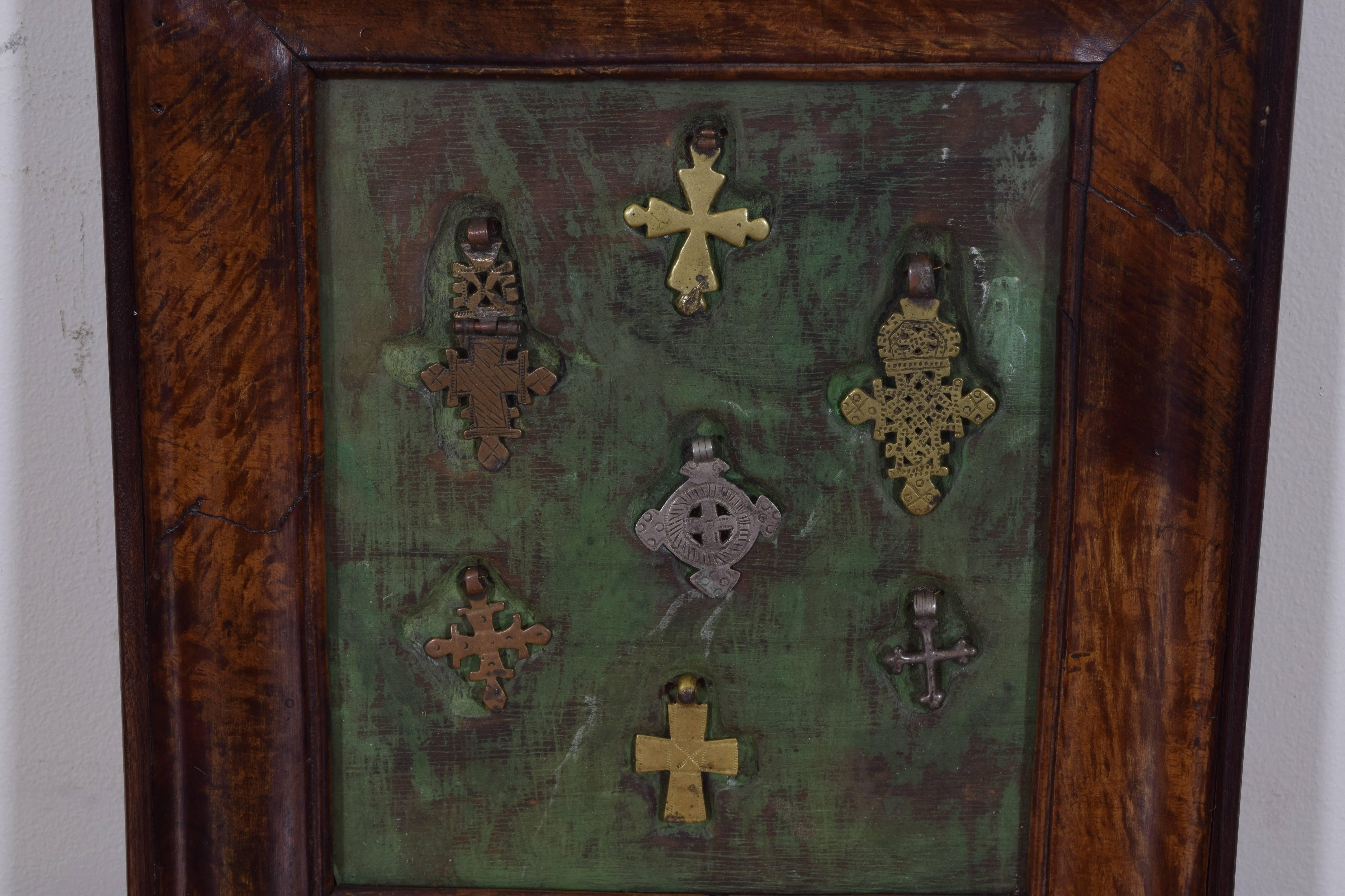 Framed in an Italian walnut frame; the crosses are suspended and recessed on a green fabric ground.