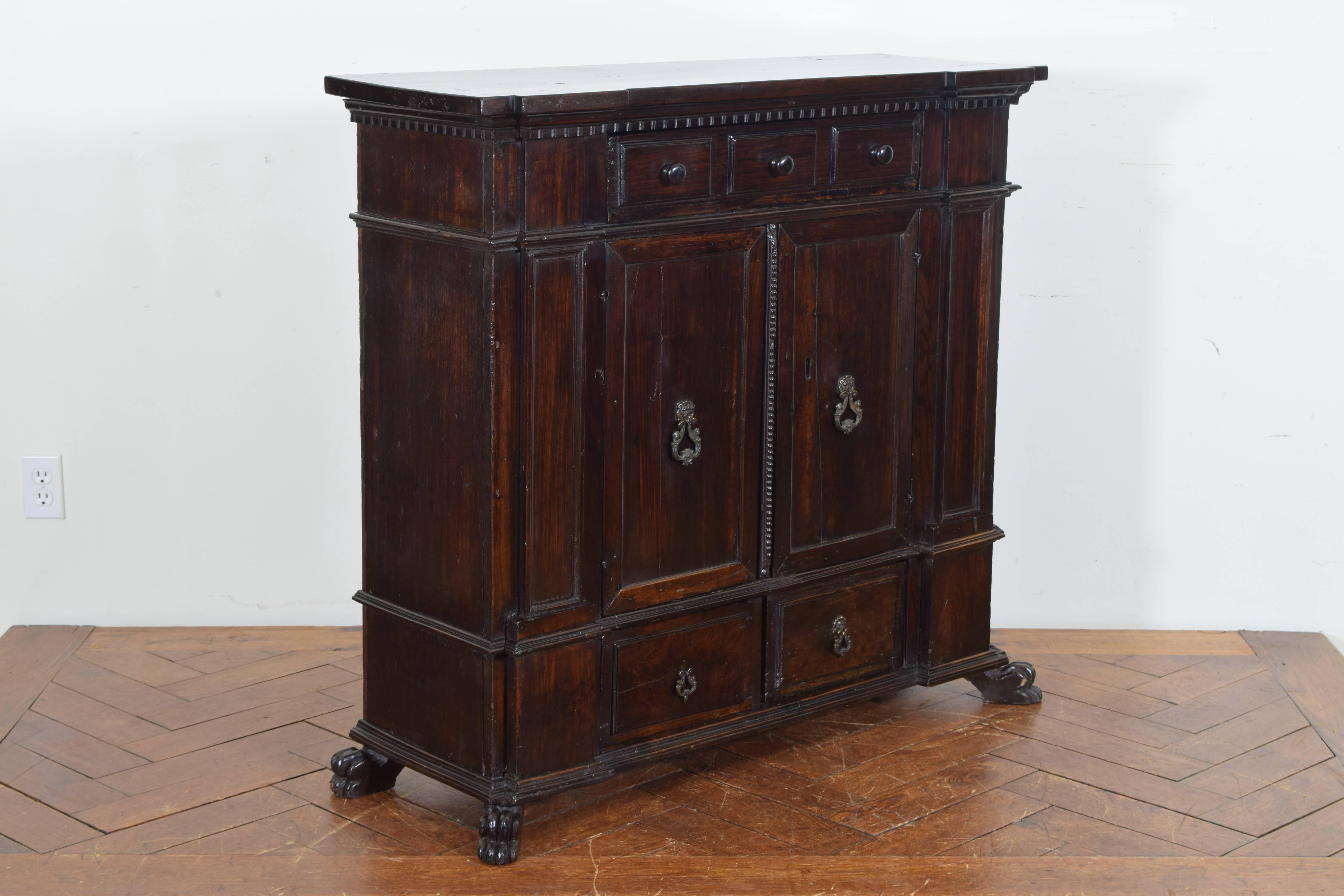 The rectangular top with notched corners and a dentile molding above a conforming shallow case housing one drawer over two doors, with pilasters flanking the doors, the lower section having two drawers, raised on splayed animal paw feet.