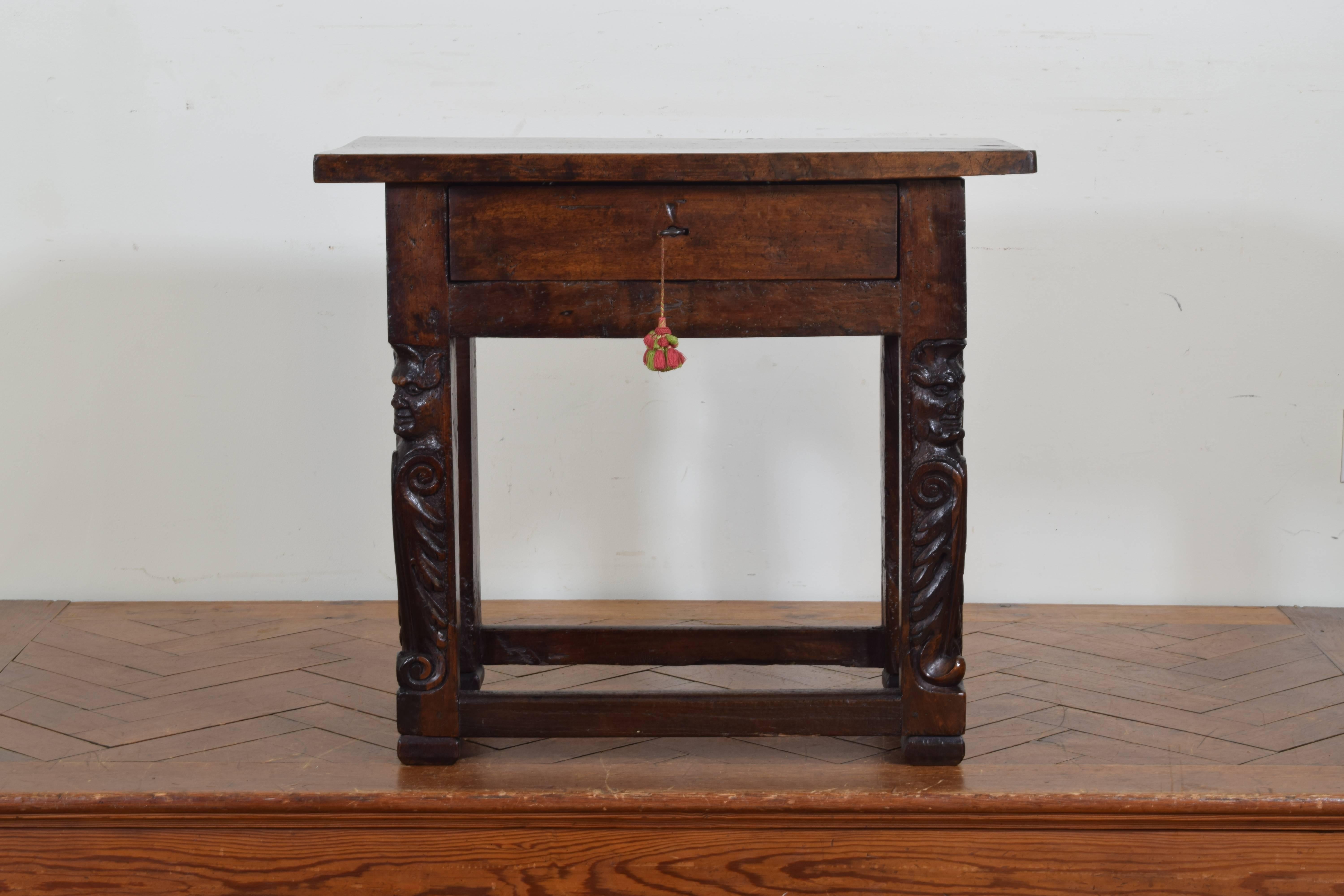 Having a solid one board walnut rectangular top above one locking drawer, the legs with carved masks and foliate details, the legs joined by a box stretcher.