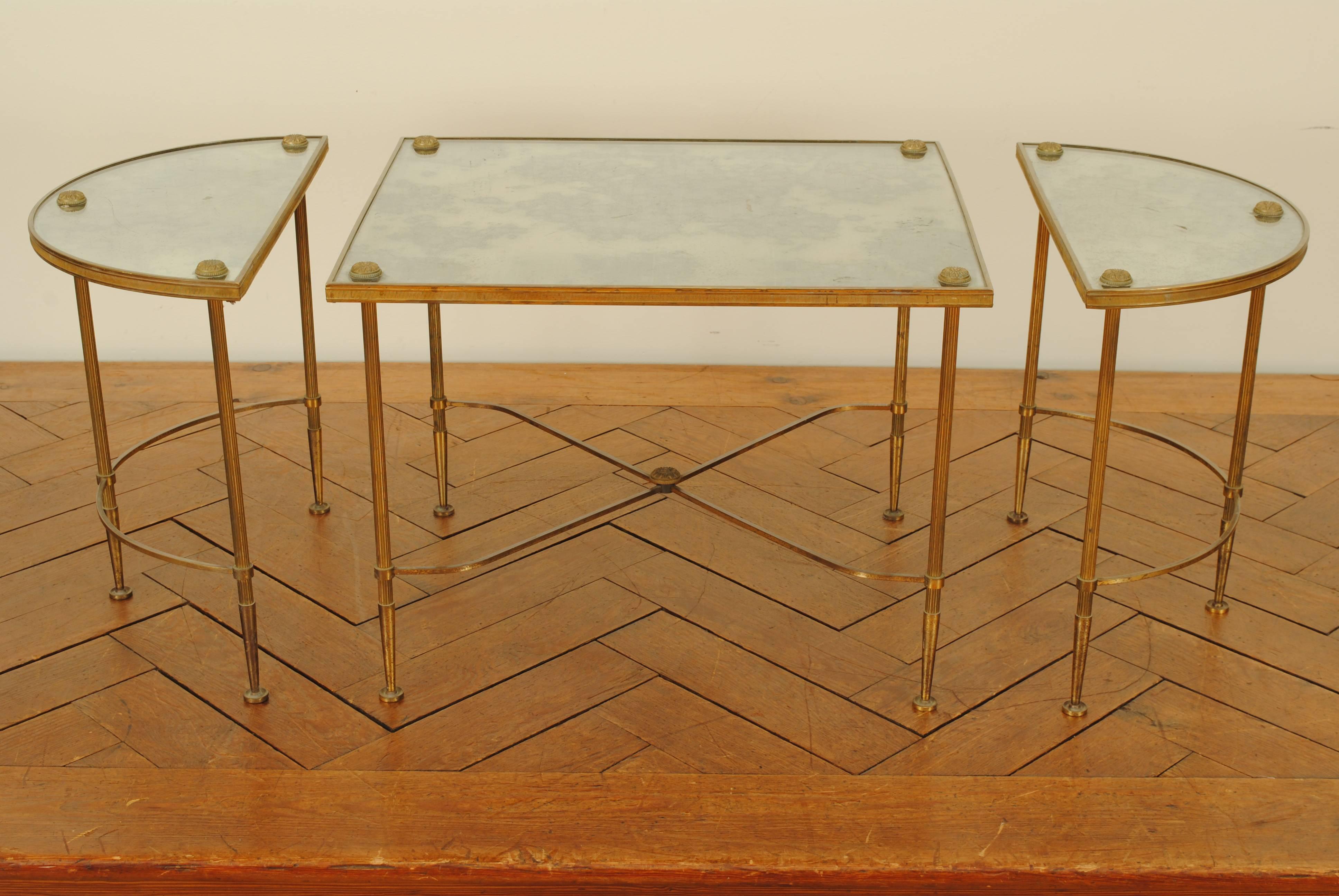 Three independent tables, two of demilune form, the center section rectangular, all with mirrored tops, all sections with raised brass corner rosettes, the straight legs tapering at the feet and joined by curved and X-form stretchers, mid-20th