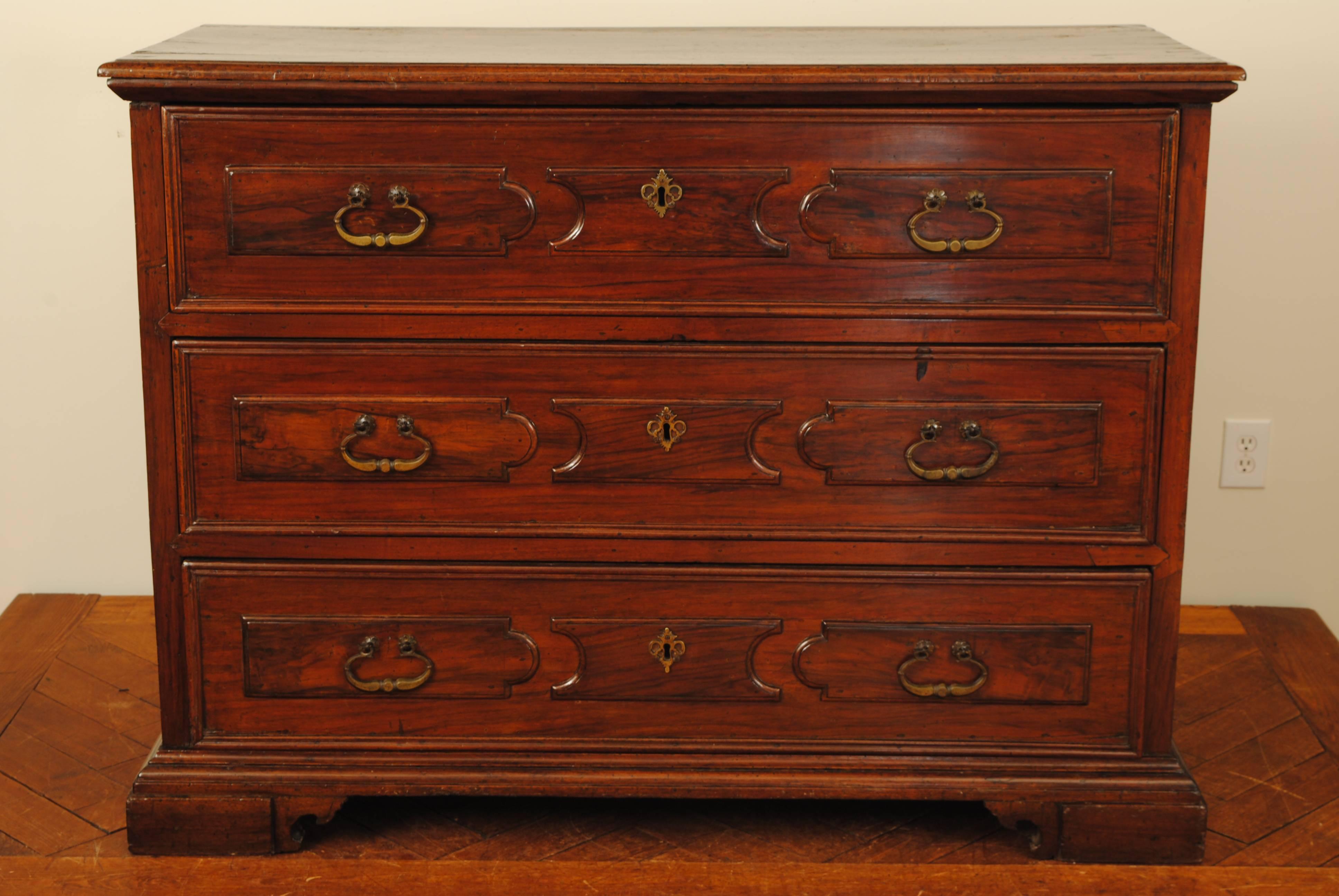 Having a molded edge rectangular top above a conforming paneled case, the drawer fronts with molded edges, raised on a plinth-form base and bracket feet, antique brass hardware.