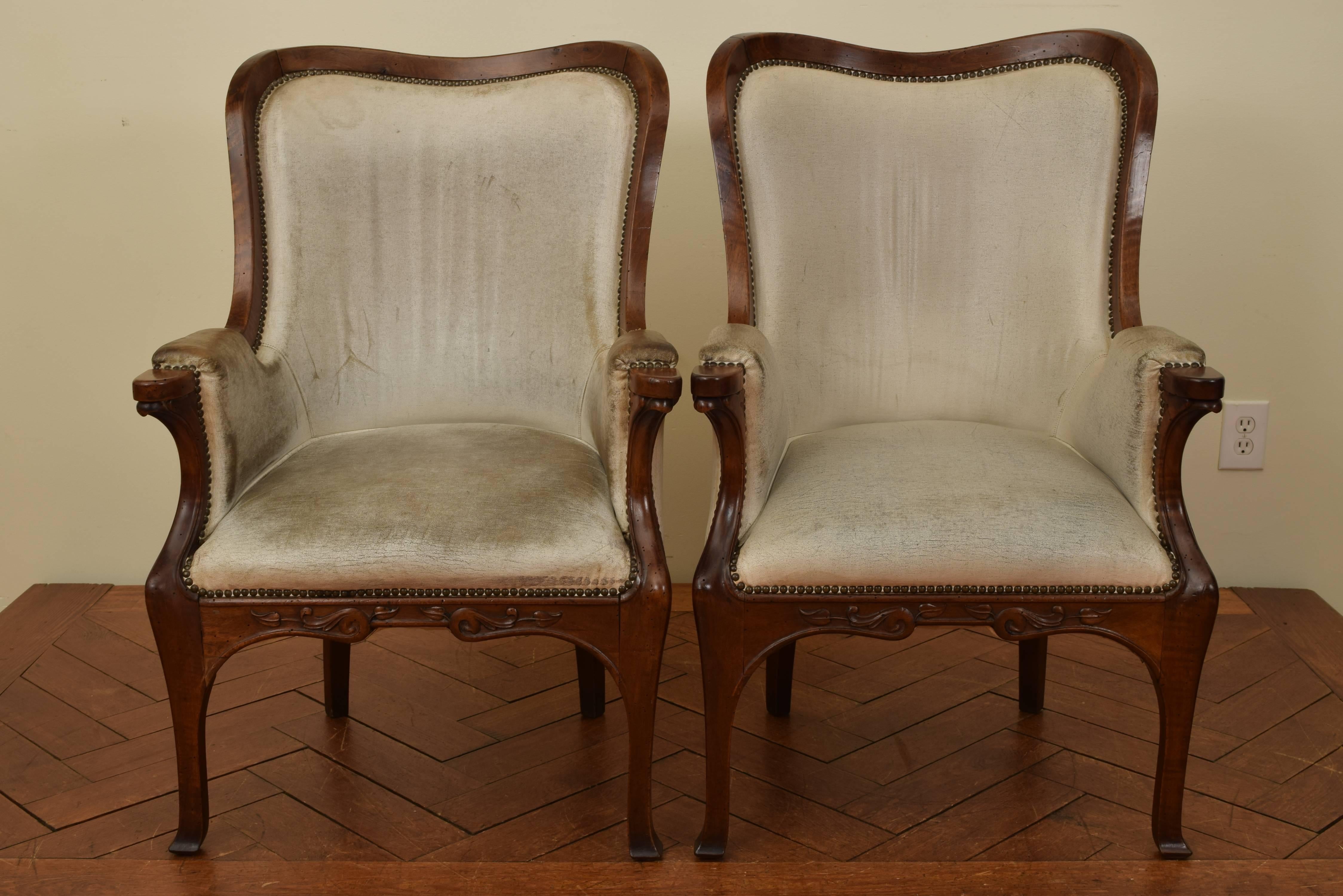 Pair of French walnut Art Nouveau bergères constructed entirely of walnut and upholstered in white leather, the concave backrests continuing to padded arms and carved handles, the front stretchers with scroll and leaf carvings, raised on slightly