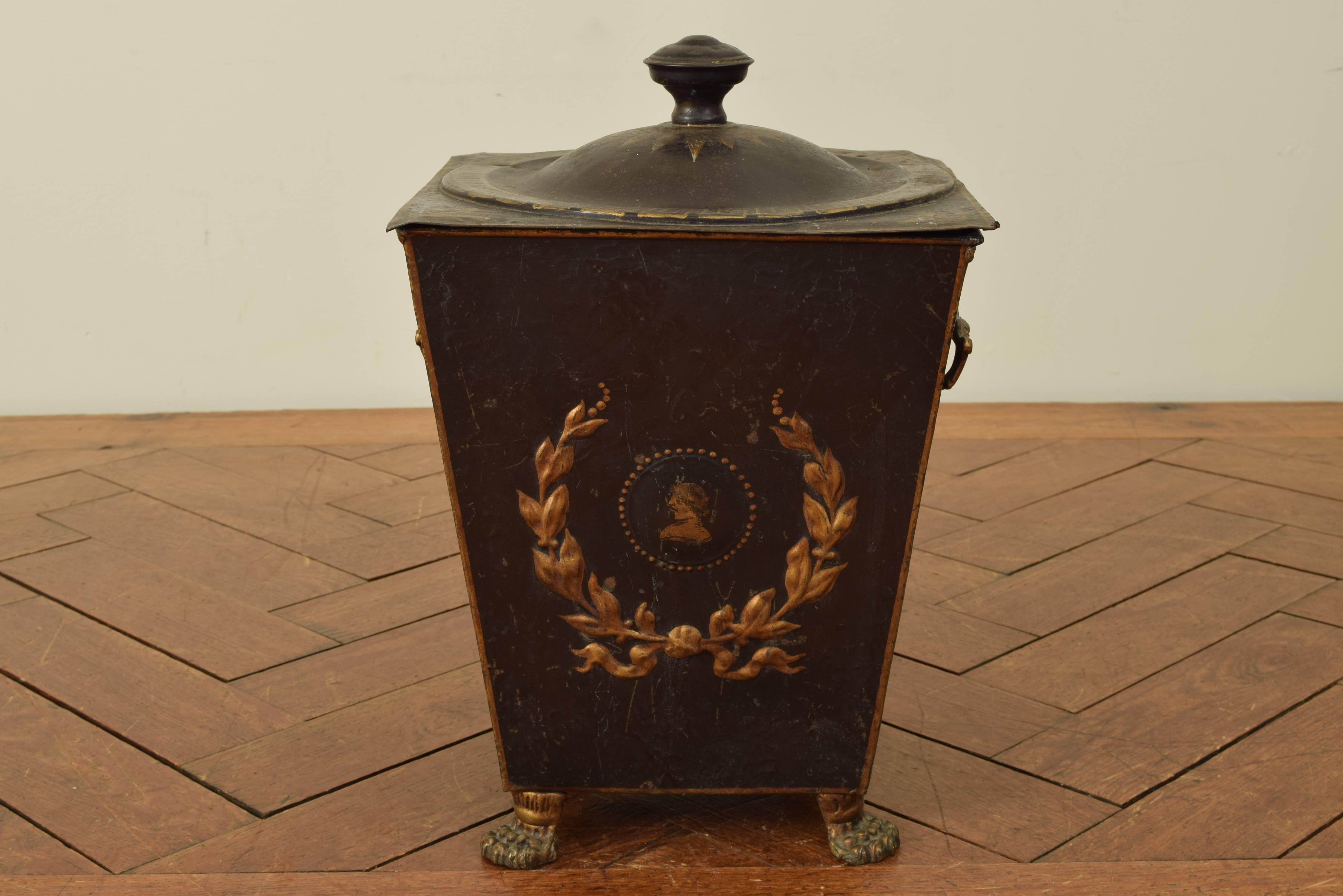 Of square tapering form, the removable top with a finial, Greek key and star painted decorations, the side with handles and painted wreaths and busts in profile, raised on cast painted metal feet.