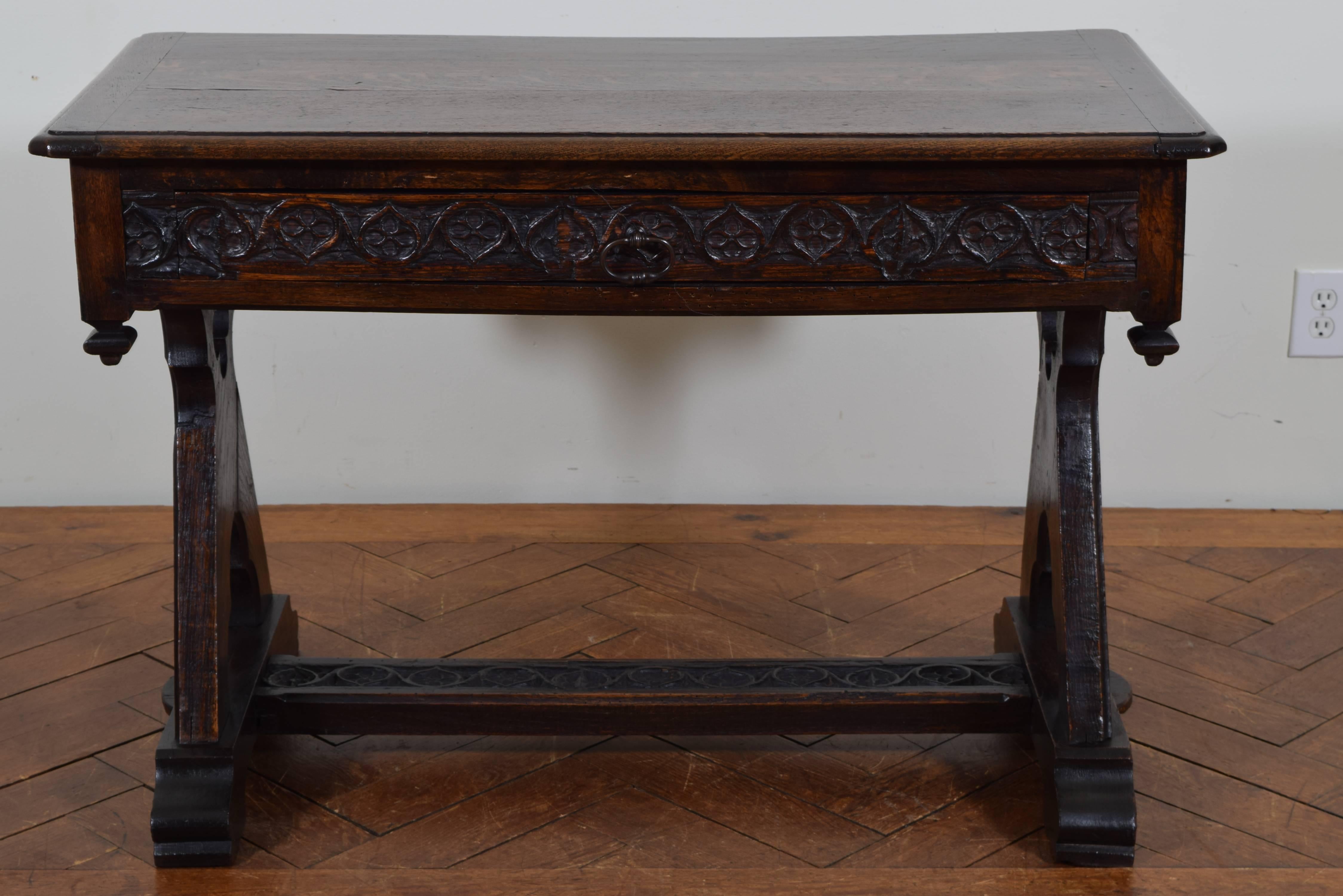 The rectangular top with molded edge above a conforming case with a heavily carved apron and drawer, the bottom with turned terminals in the corners, raised on carved trestle supports with pierced quatrefoil carvings, the legs joined by a carved