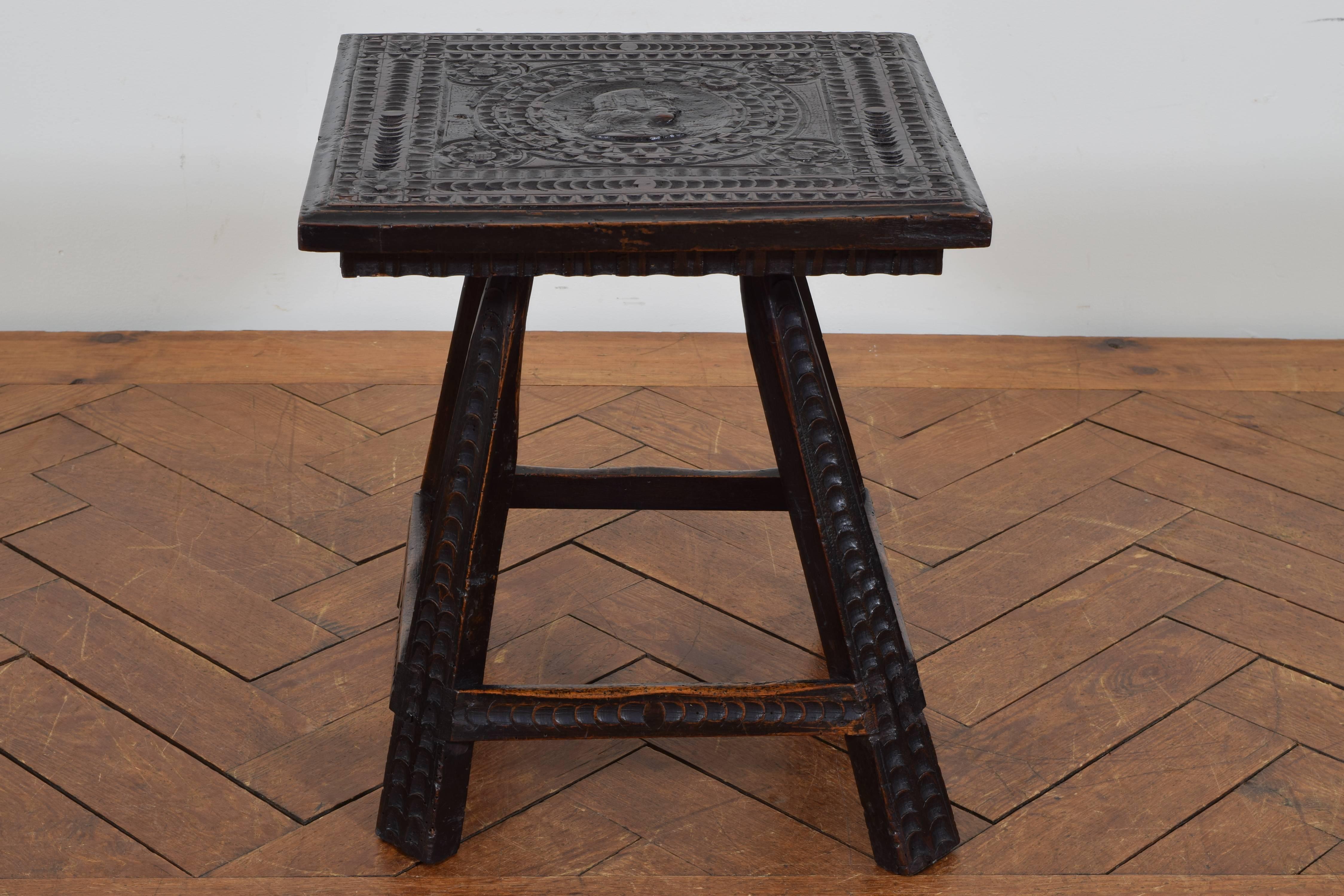 The square top carved with a central figure in profile, raised on slanted legs joined by a square stretcher.