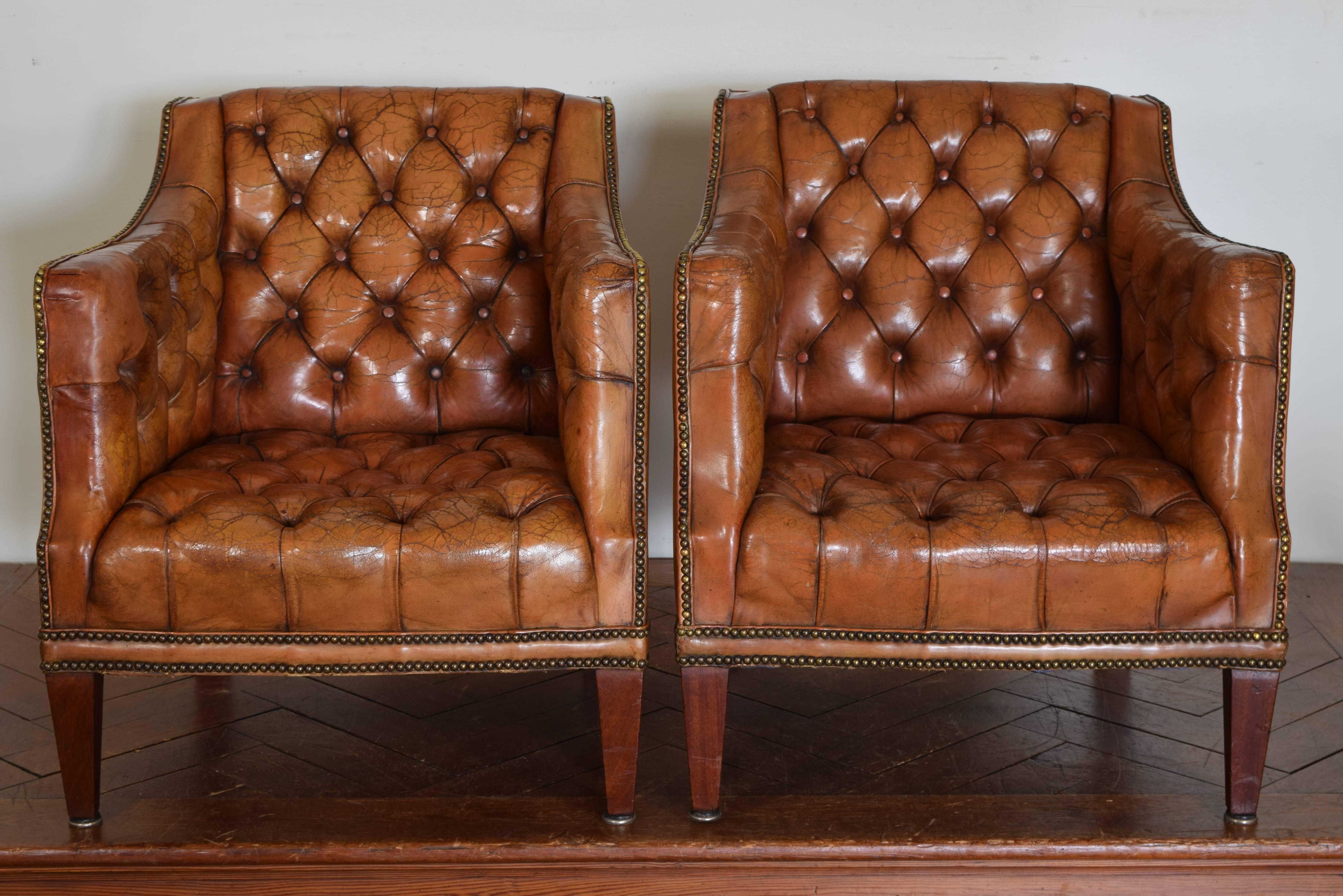 From the first half of the 20th century, having square back and shaped sides, the interiors upholstered in tufted leather, the sides and back panels upholstered in leather, trimmed in patinated brass nailheads, raised on square tapering legs.