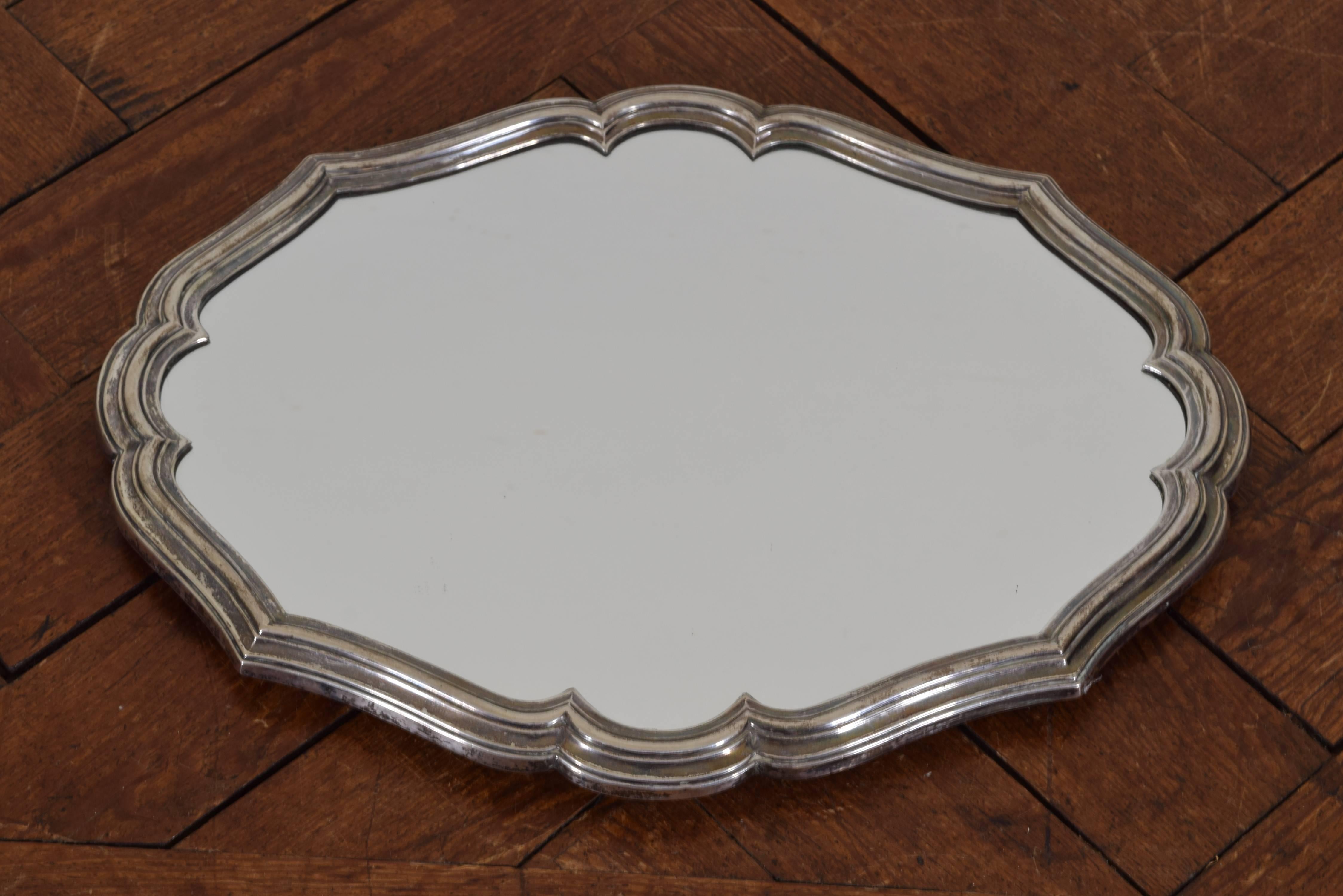 Silver plated mirrored tray of Rococo form with a molded edge and having a wooden frame and small shaped feet.