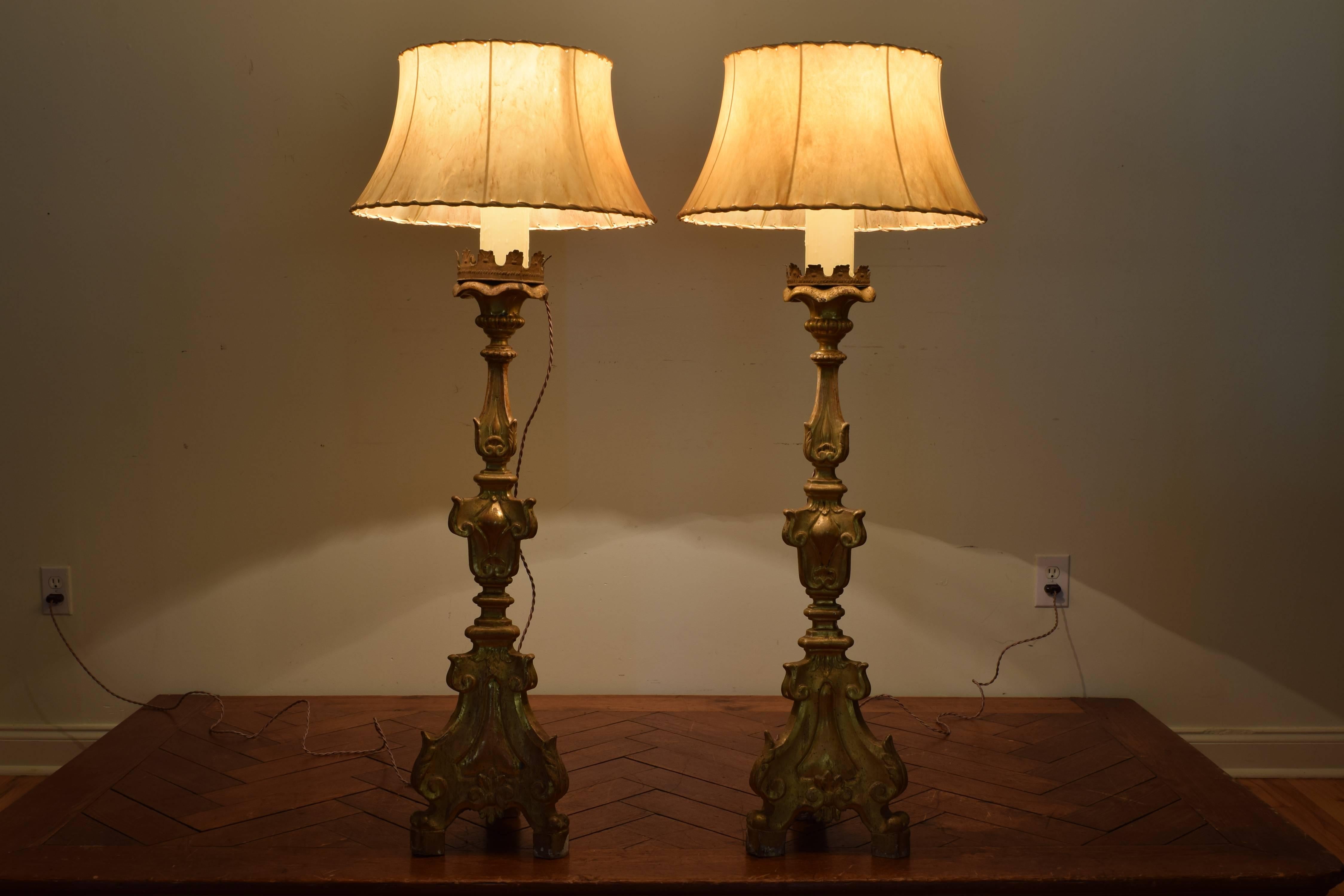 Photographed with hide shades the metal drip pans resting atop two-piece carved and gilded candlesticks, now outwired for electricity. Measurements listed include shades. Height to top of metal drip pans is 38 inches; diameter of candlestick bases
