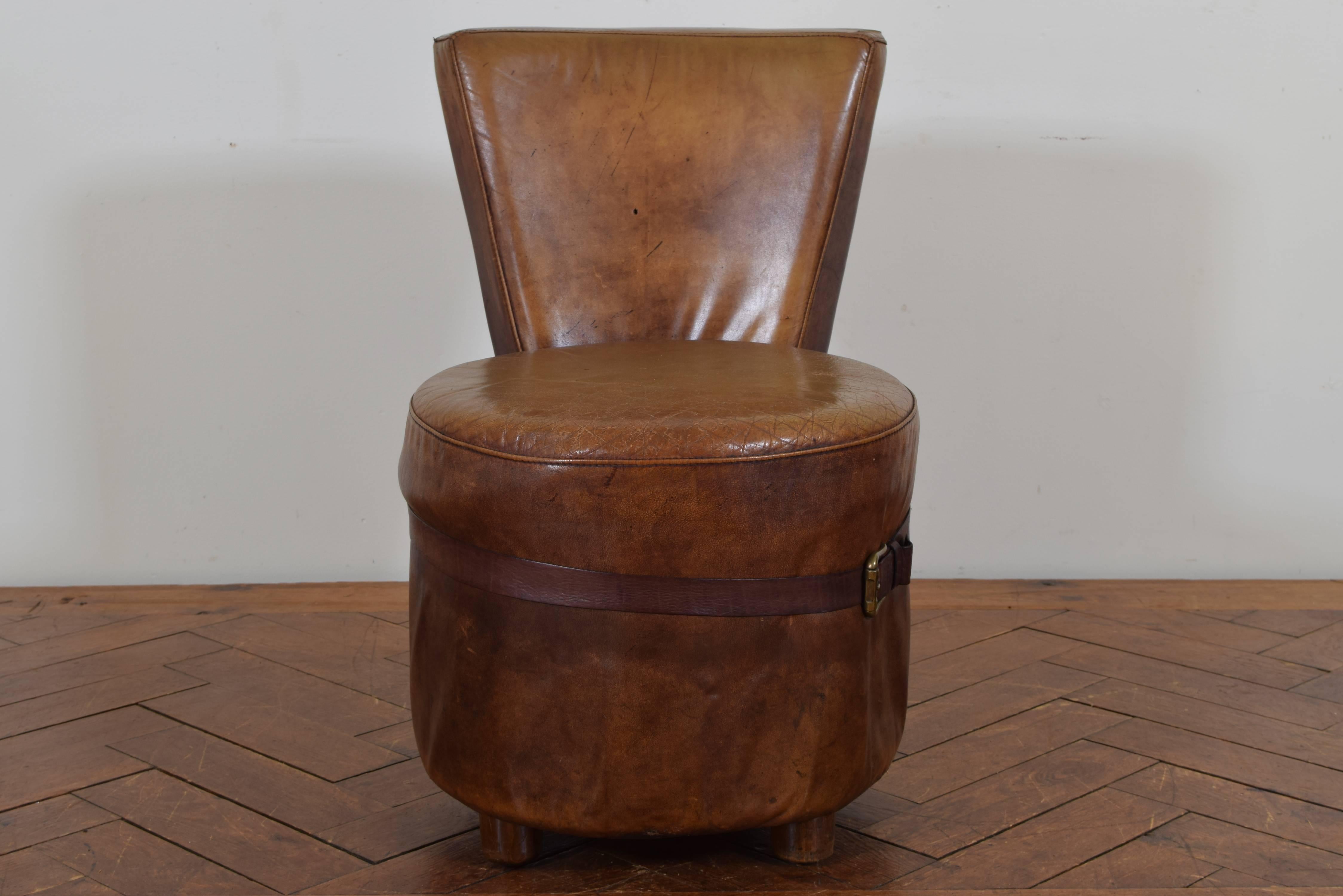 The v-shaped backrest is concave and trimmed in brass nailheads, the seat portion essentially a round poof and decorated with a leather belt inscribed 