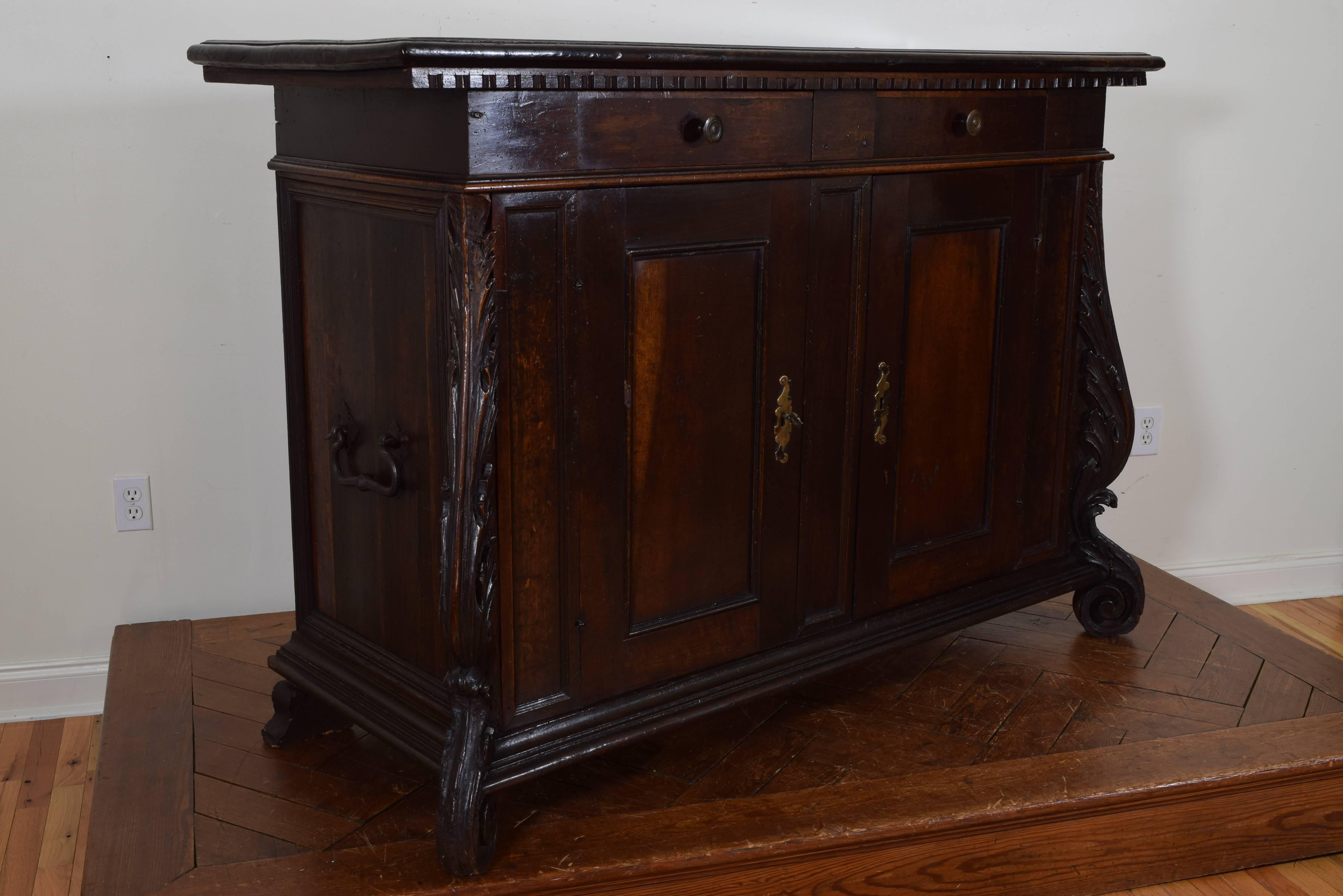 The rectangular top with a dentile molded edge, two drawers over two doors, interesting carved feet extending to nearly the top, wrought iron handles at sides.
