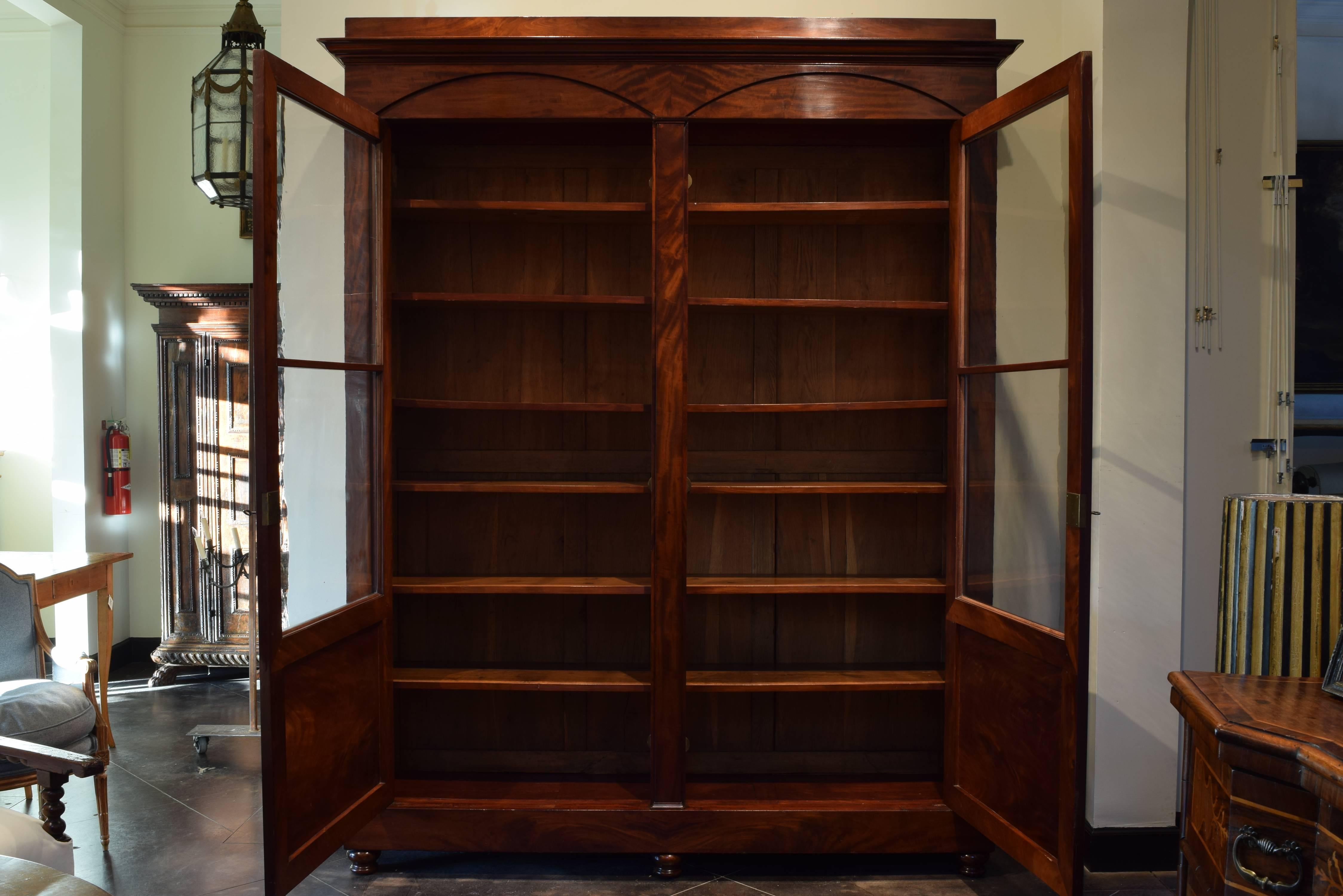 Tall and shallow, this cabinet constructed of solid mahogany and mahogany veneer, the upper section having a projecting cornice above two doors with lozenge shaped lower panels and original glass fronts, retaining original shelving and brass