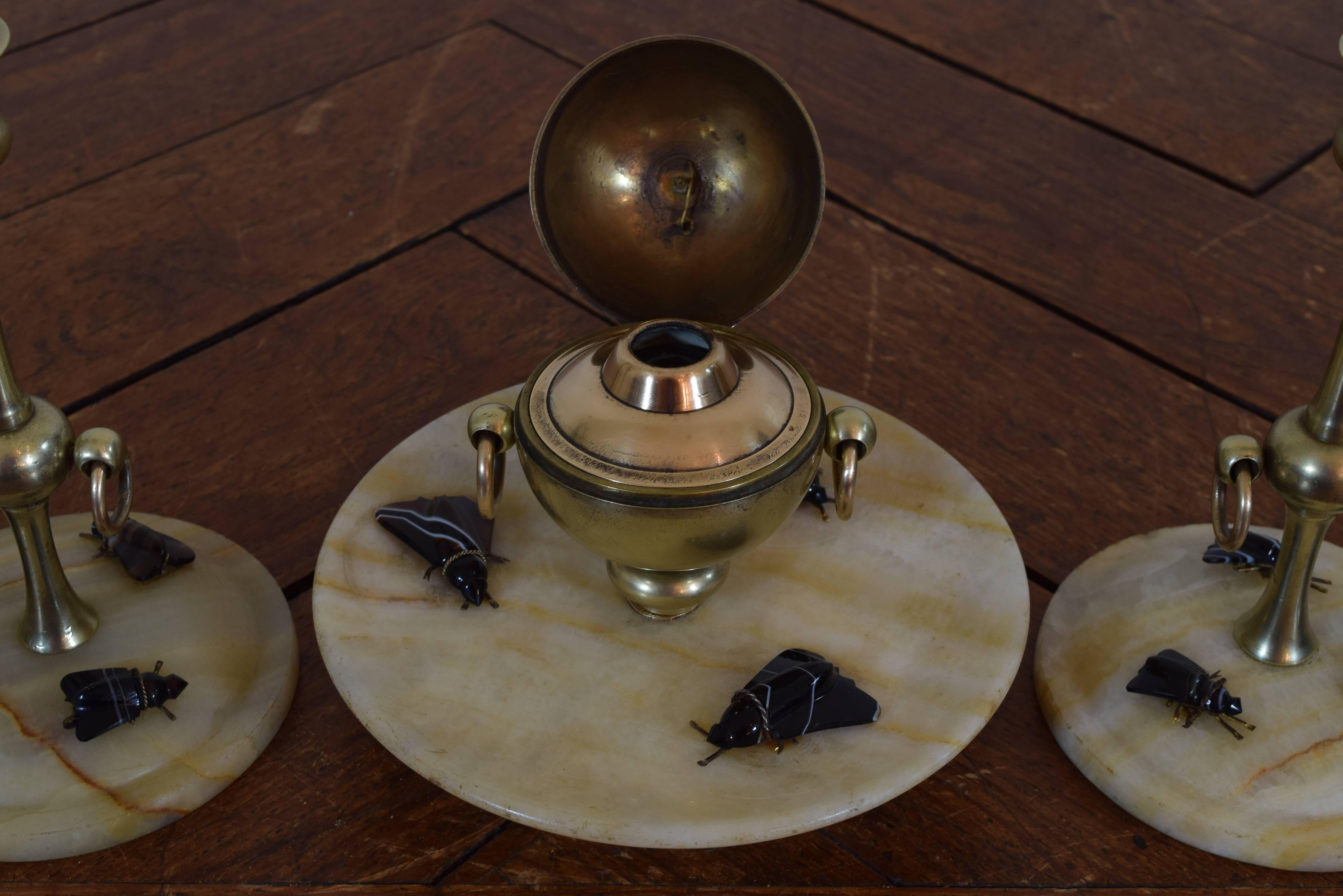 The inkwell having domed and hinged lid with brass rings with a lower tray of agate decorated with dark agate flies, resting on a brass base.  the candlesticks of slender proportion and having same brass handles, the agate bases decorated with dark