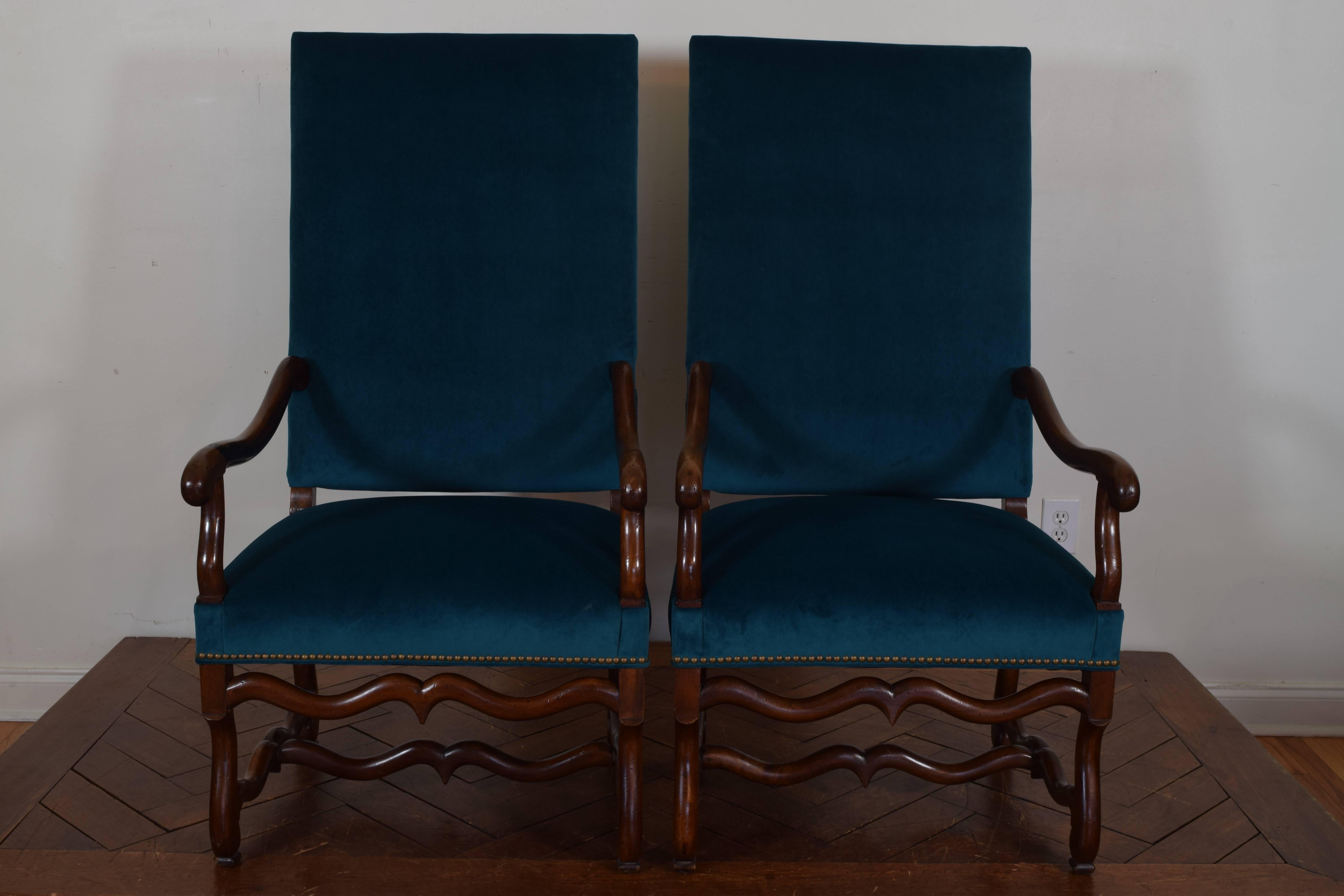 Having upholstered seats and backs with curved arms, stretchers and legs in the Os de Mouton style of the early 18th century, these armchairs from the mid-19th century, upholstered in velvet trimmed in patinated brass nailheads.
