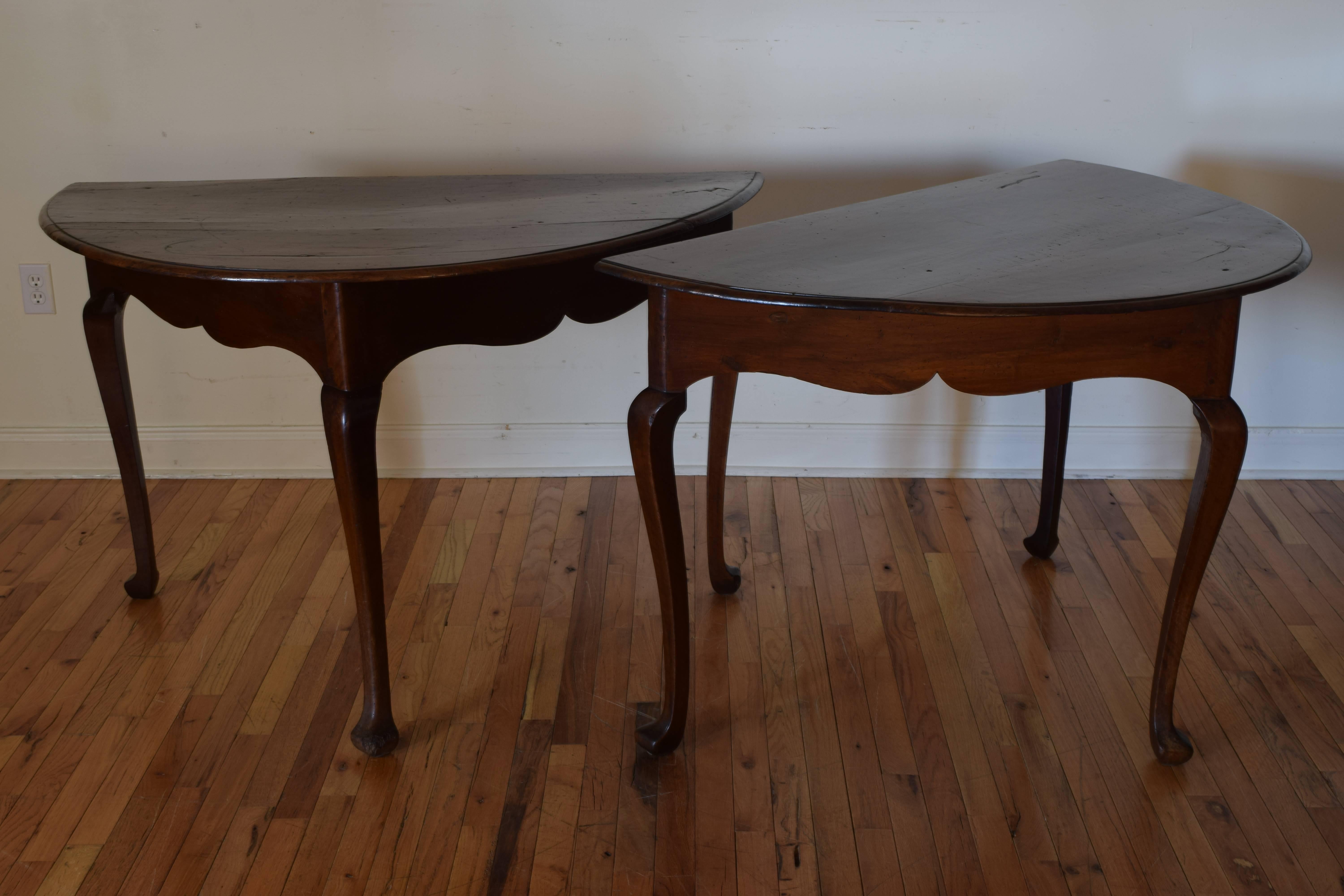 Actually half-oval as opposed to demilune in shape the pair of tables can be joined to make a larger table, constructed entirely of solid walnut and having shaped aprons raised on cabriole legs with shaped feet borrowing from the earlier English