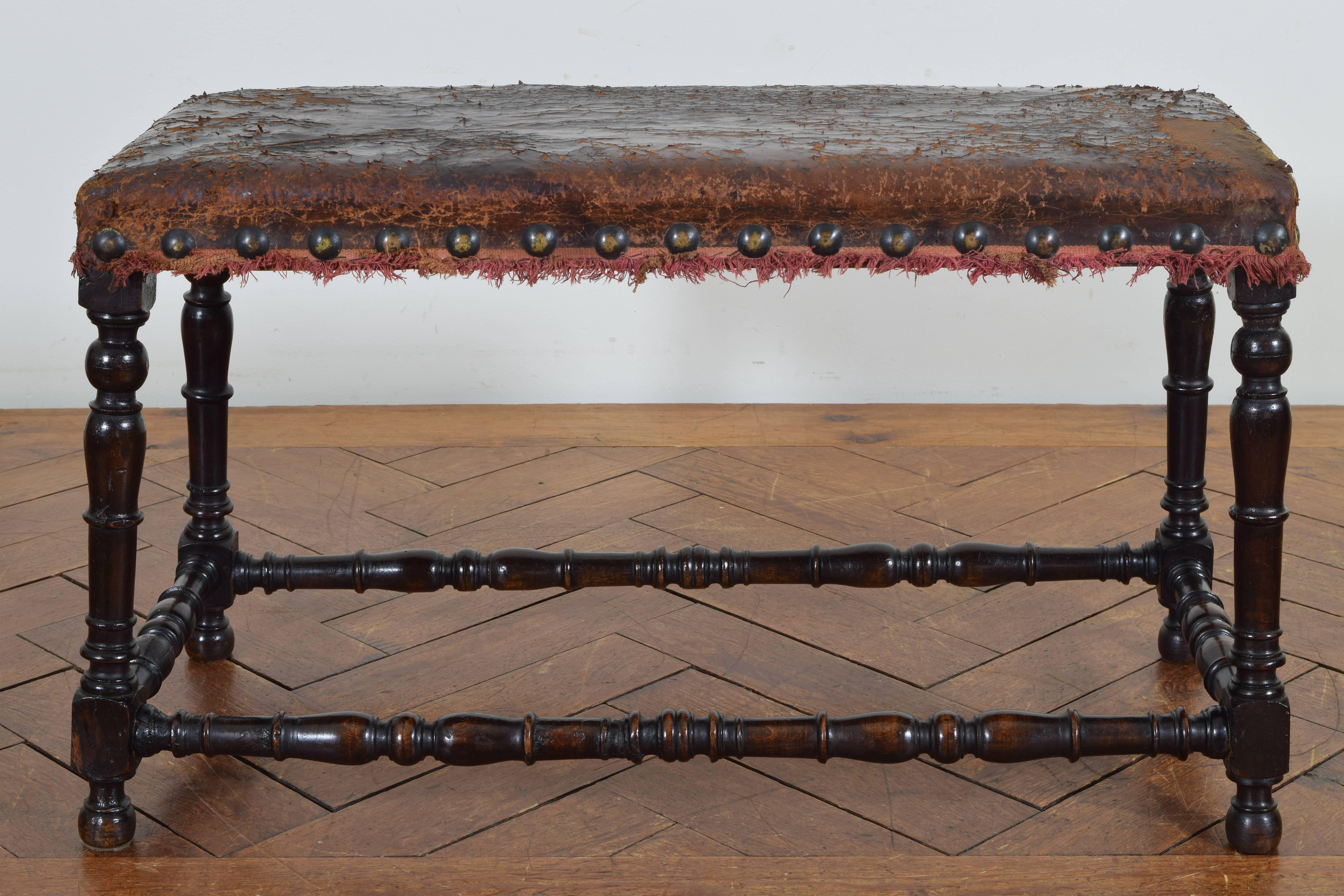Of rectangular form and retaining antique leather with nailheads and fringe, raised on turned legs connected by turned stretchers, ball feet.