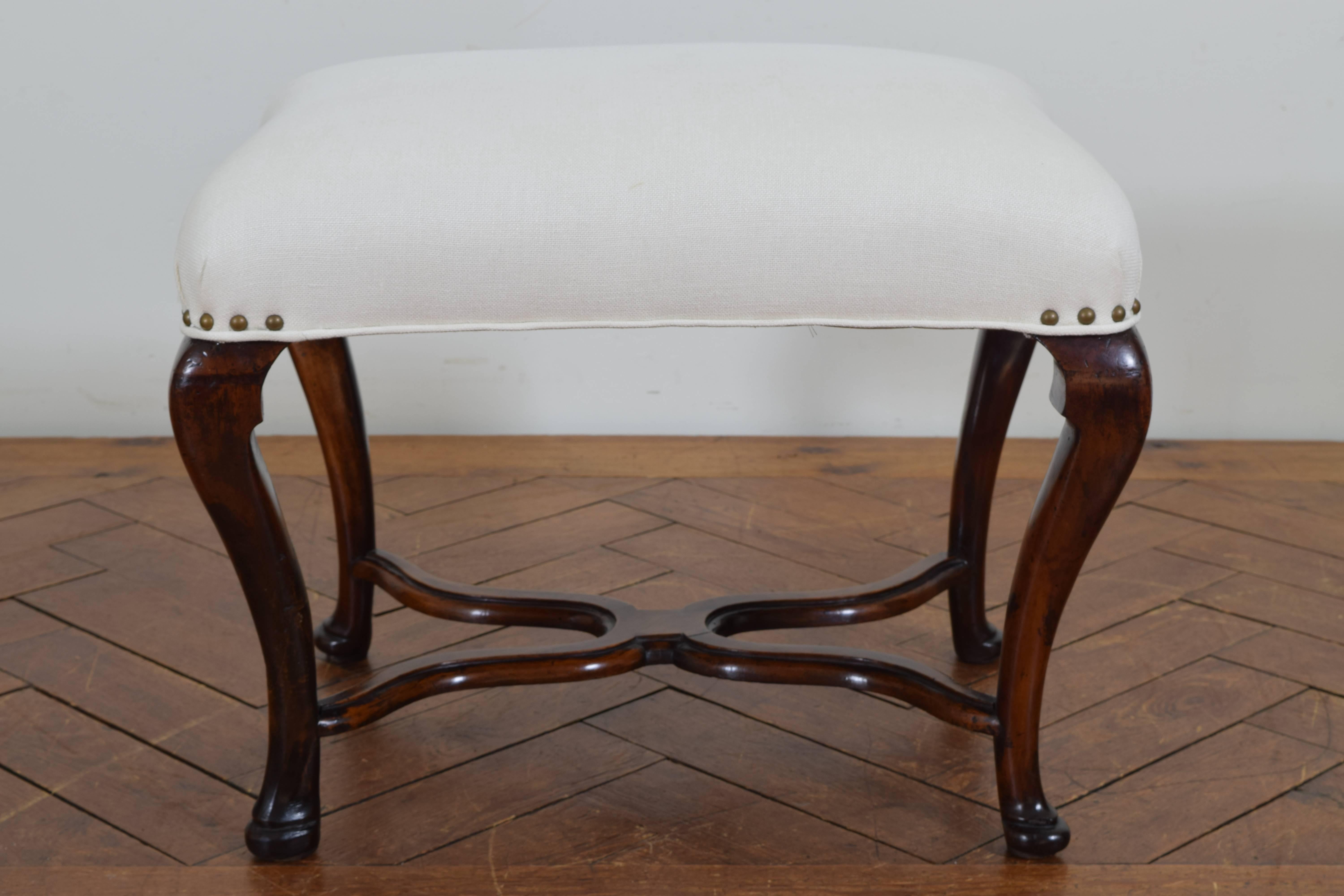 Having a shaped top upholstered in white linen and trimmed in nailheads, supported by cabriole legs joined by a shaped X-form stretcher, the legs ending in pad feet.