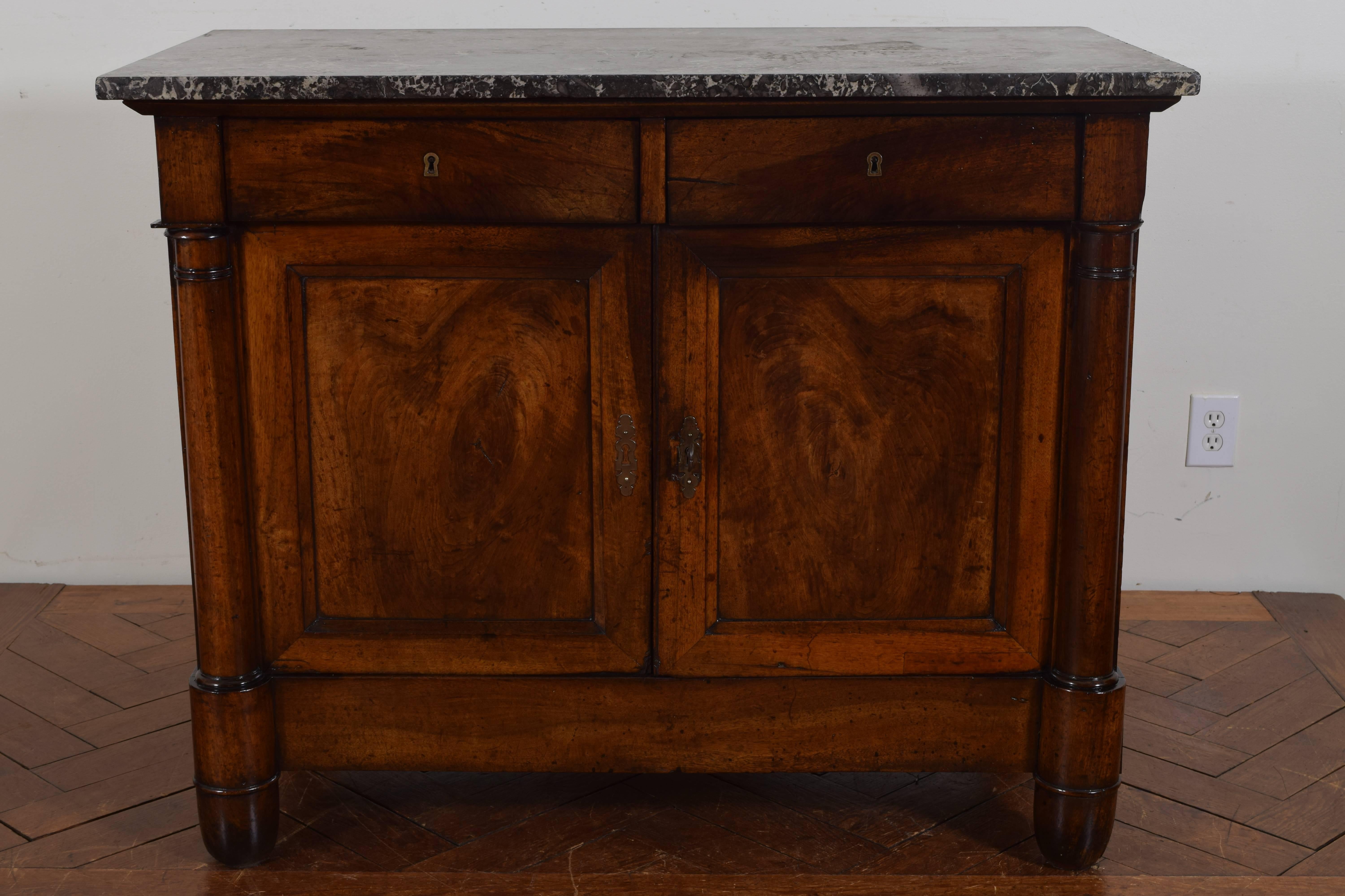 Having a rectangular dark grey and white marble top, with two drawers over two doors, columnar decorations at front with rounded feet, second quarter of the 19th century.
