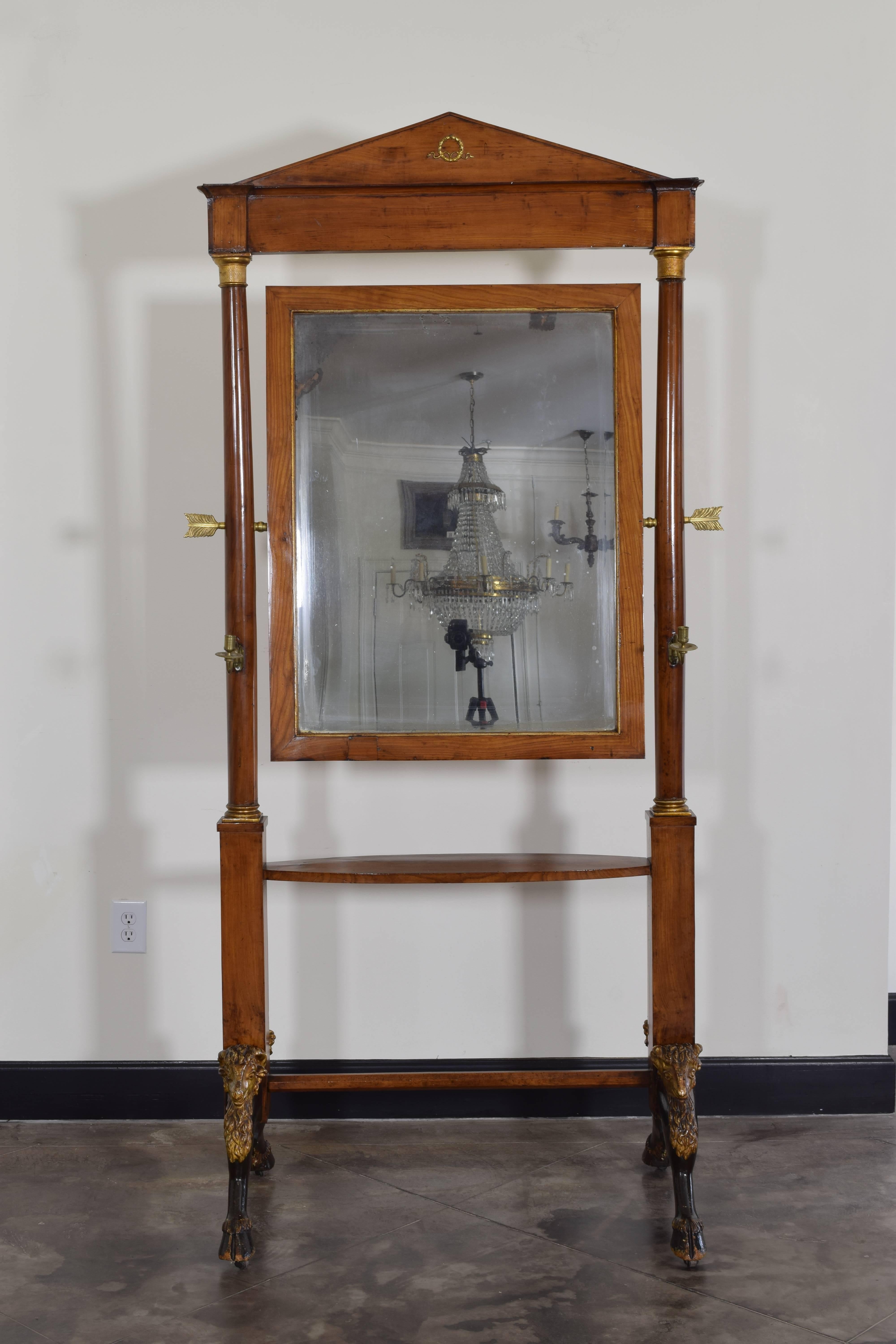 important and rare and completely intact, retaining antique beveled mirrorplate, the pivoting mirror held in place within the columned frame by brass arrow parts, the frame surmounted by a neoclassical pediment adorned with brass decoration, below