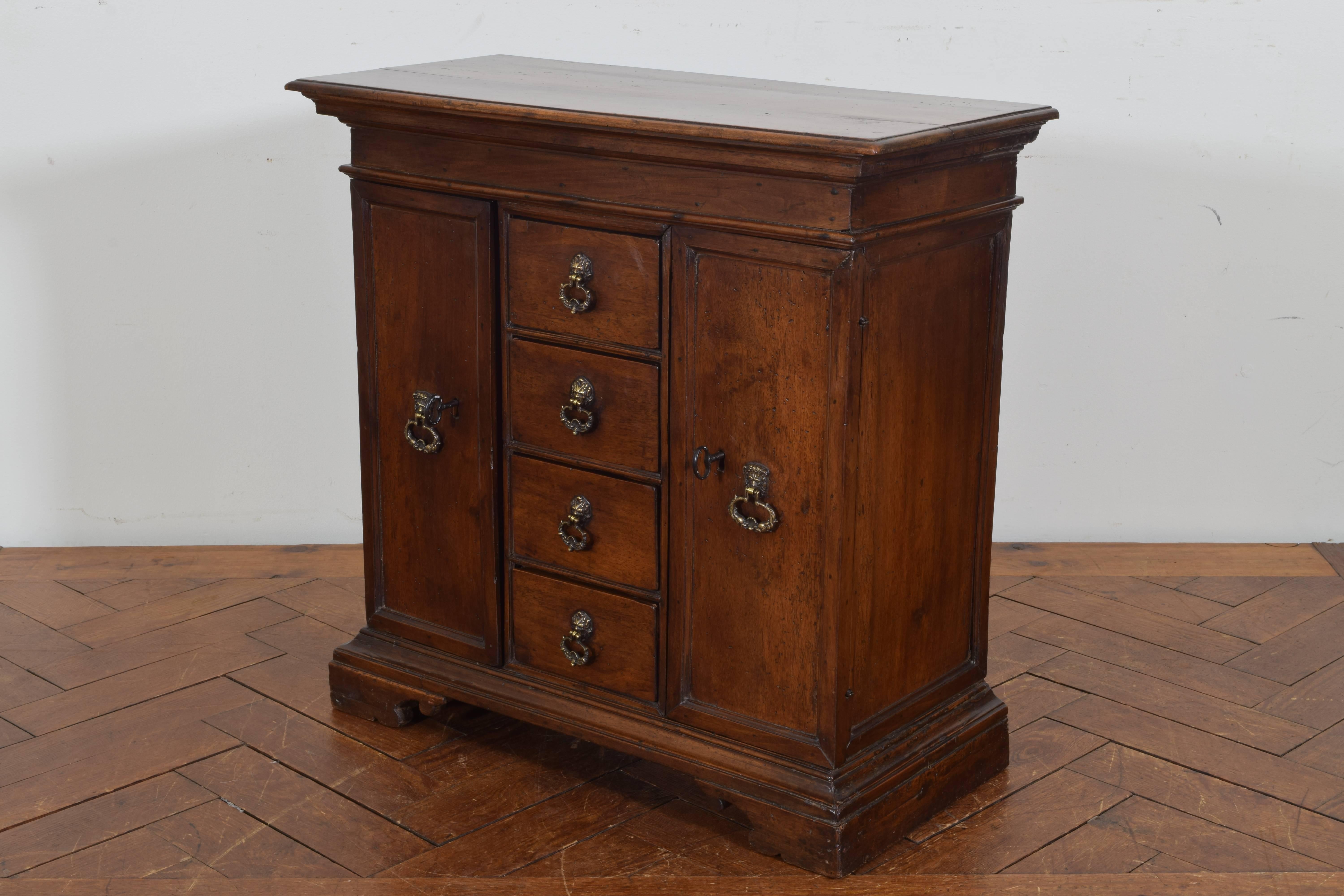 In perfect condition and interestingly constructed with four central drawers and two side doors, the rectangular top above a conforming case raised on bracket feet, having lion mask hardware and original locks and keys.