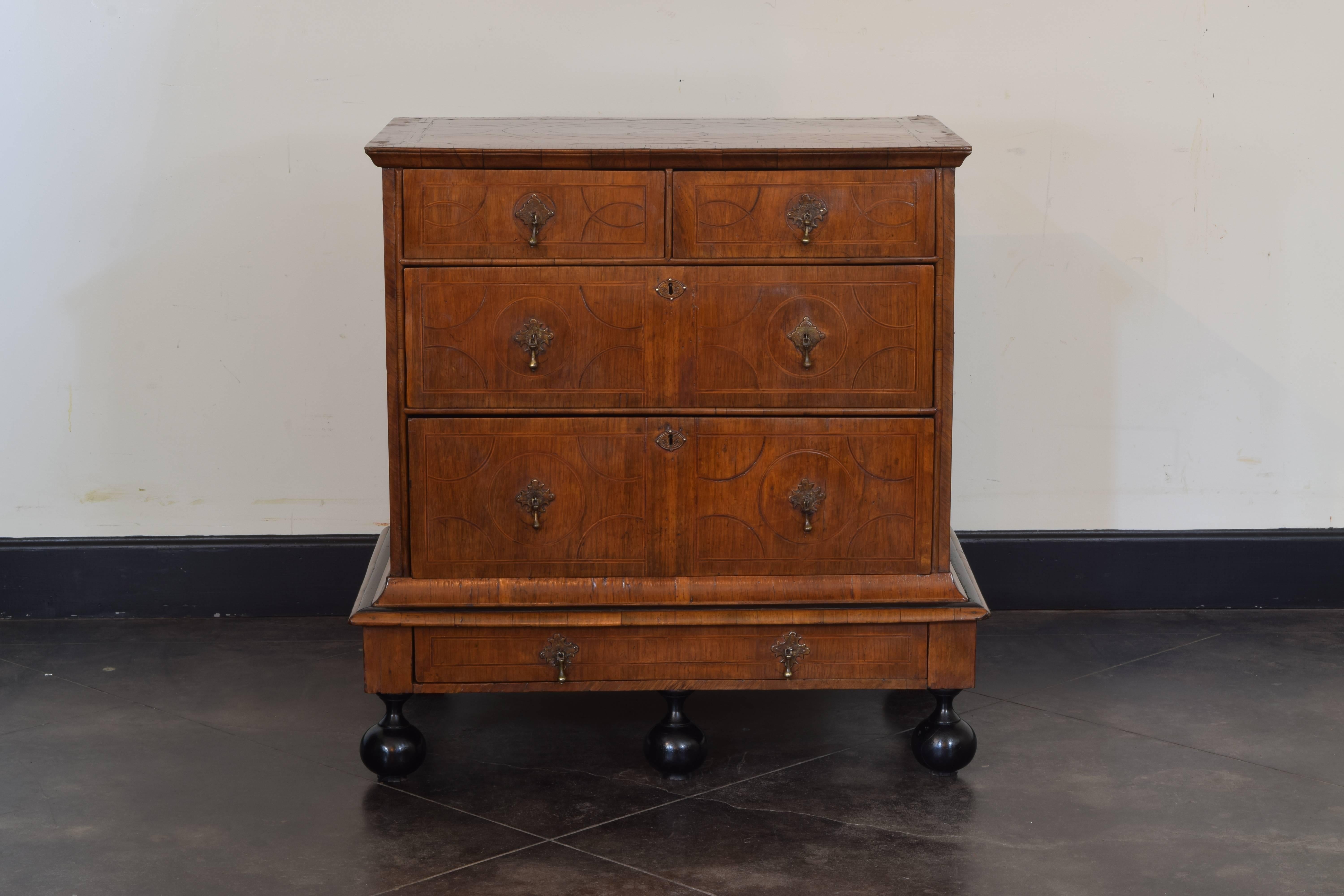 Elaborately veneered with circular and oval bands of inlay, the top with a chamfered edge above a similarly veneered case housing two smaller drawers over two larger drawers, resting on a veneered base housing one drawer and raised on large ebonized