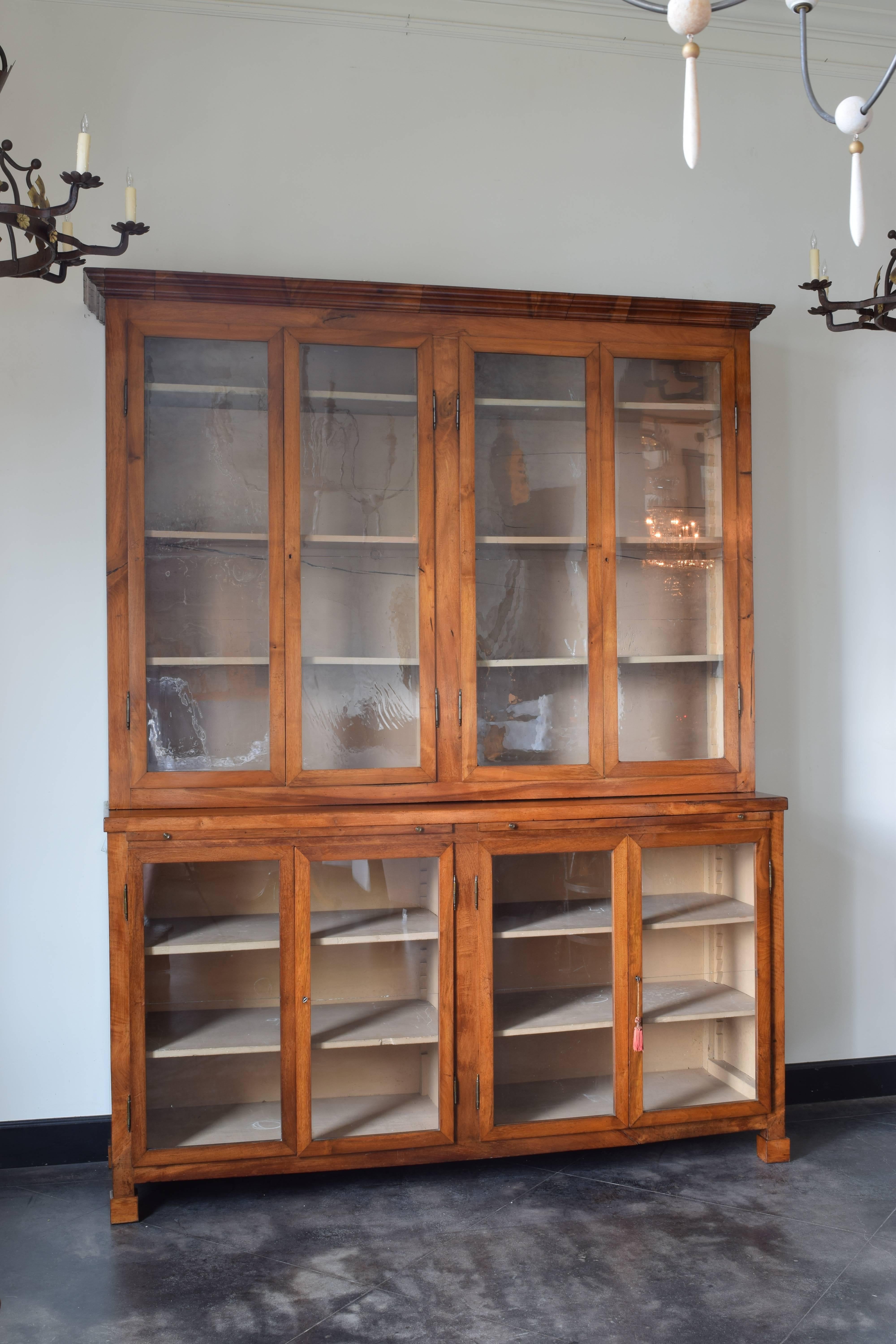 Wonderful and rare bookcase from a library in the Veneto region of Italy, of two piece construction having upper sections with molded crowns and two separate shelving areas enclosed by glass doors, the lower sections, of slightly greater depth,