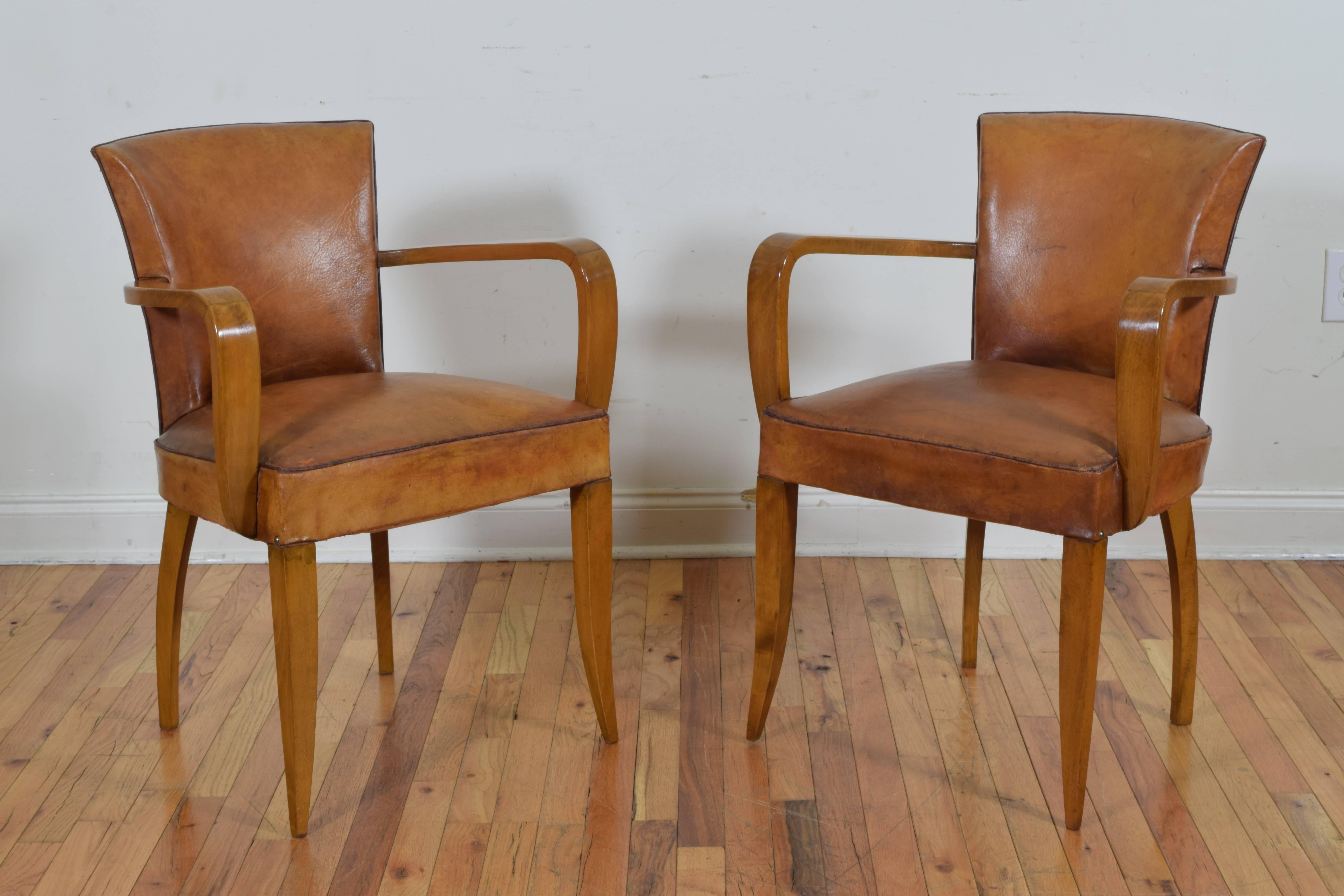 having concave backrests, curved wooden arm supports, flared legs, the leather upholstery in excellent condition and trimmed in a darker leather piping with nailheads on the back of the backrests