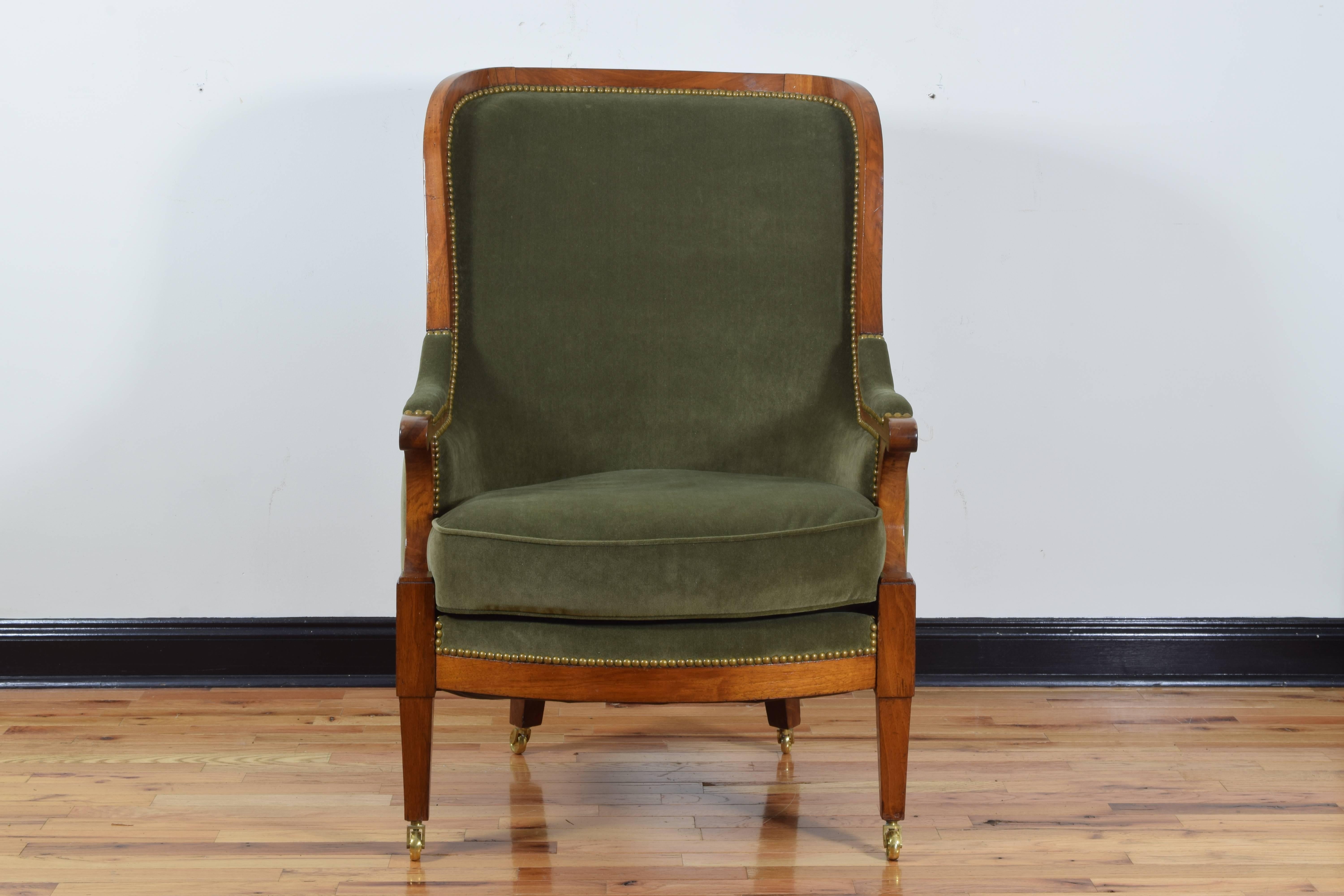Of large proportion and having a concave backrest and enclosed arms, the upper portion of the arms with upholstered pads, all of the velvet upholstered areas trimmed in brass nailheads, having interesting scoop shaped arm supports and raised on