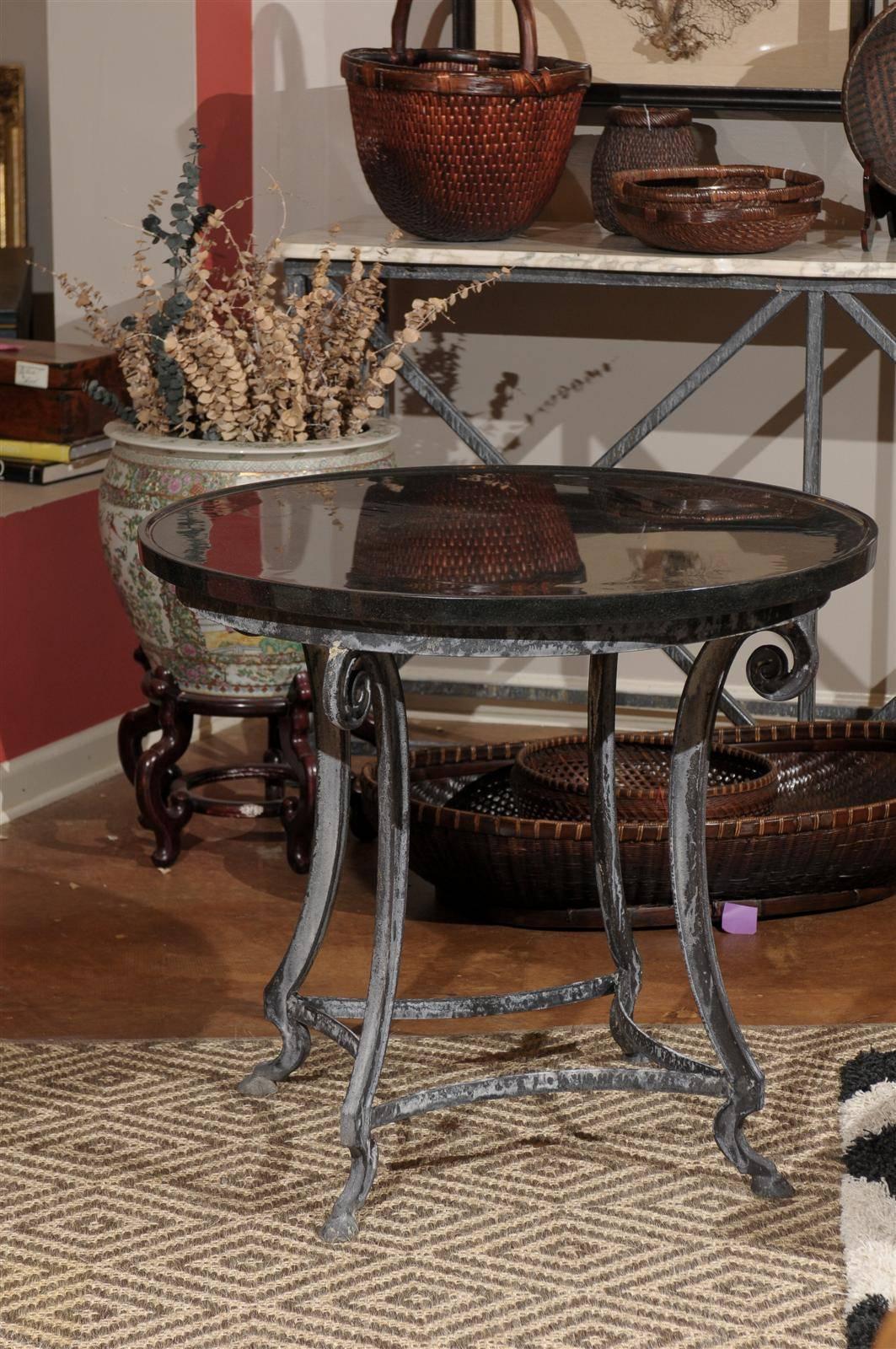 This is a lovely black granite round table has an indented edge to catch the wine spills! It sits on a beautiful forged iron base that has scrolling just below the iron edge and follows down to a great looking one toed hoof. 
The iron finish is the