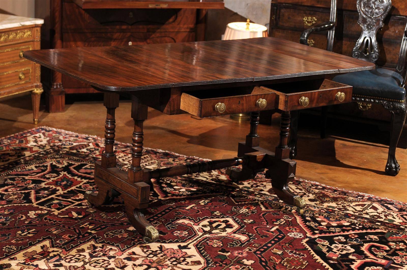 A beautiful table with a rectangular top with D-shaped drop leaves and reeded edge. Two drawers with opposing faux drawers on double pedestal. Trestle base with brass cups and casters unified by block and ring turned stretcher. The table is 57 in.