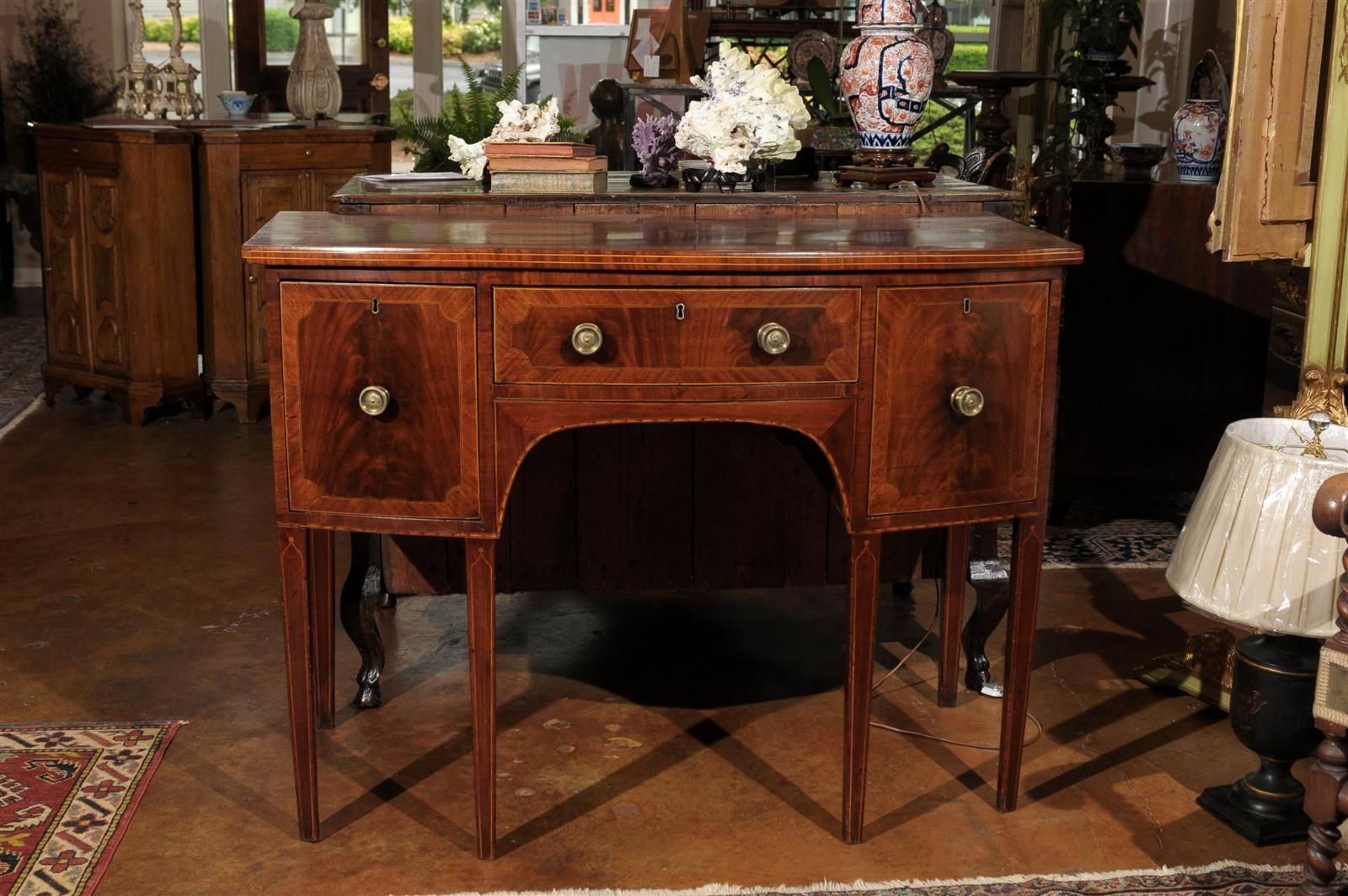 This sideboard has a shaped top over conforming case with a center drawer and two deep side drawers. Tapered legs, line inlay and quadrant corners.