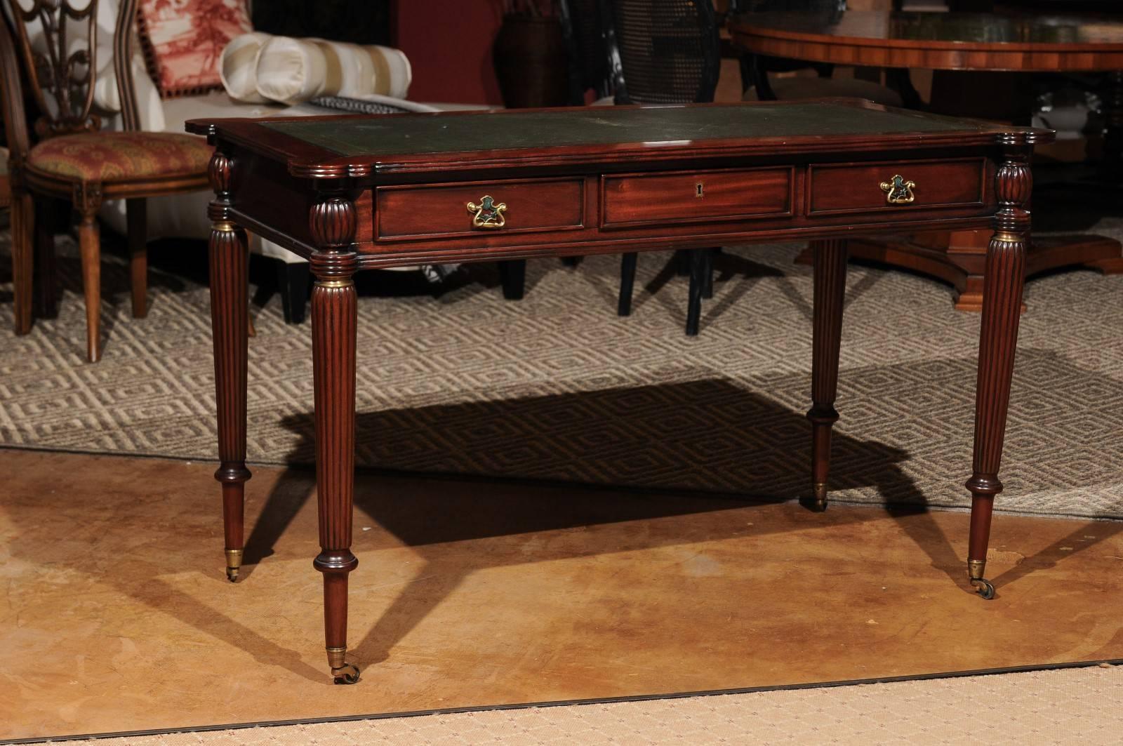 A lovely reproduction writing table with gilt tooled leather top and scalloped rounded corners. Three faux drawers on the back and three functional drawers on the front (all with brass pulls) lets it float in a room. Legs are reeded and fluted