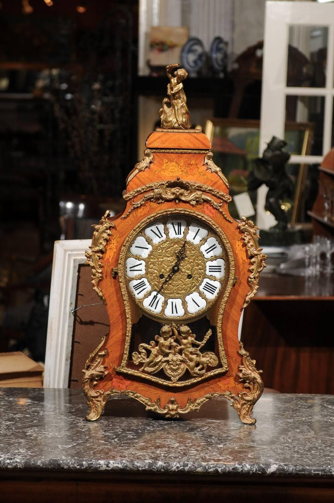 A beautiful ornate French Louis XV marquetry kingswood mantle clock with a bronze cherub on top and bronze mounts throughout. It is in working condition and chimes every hour.