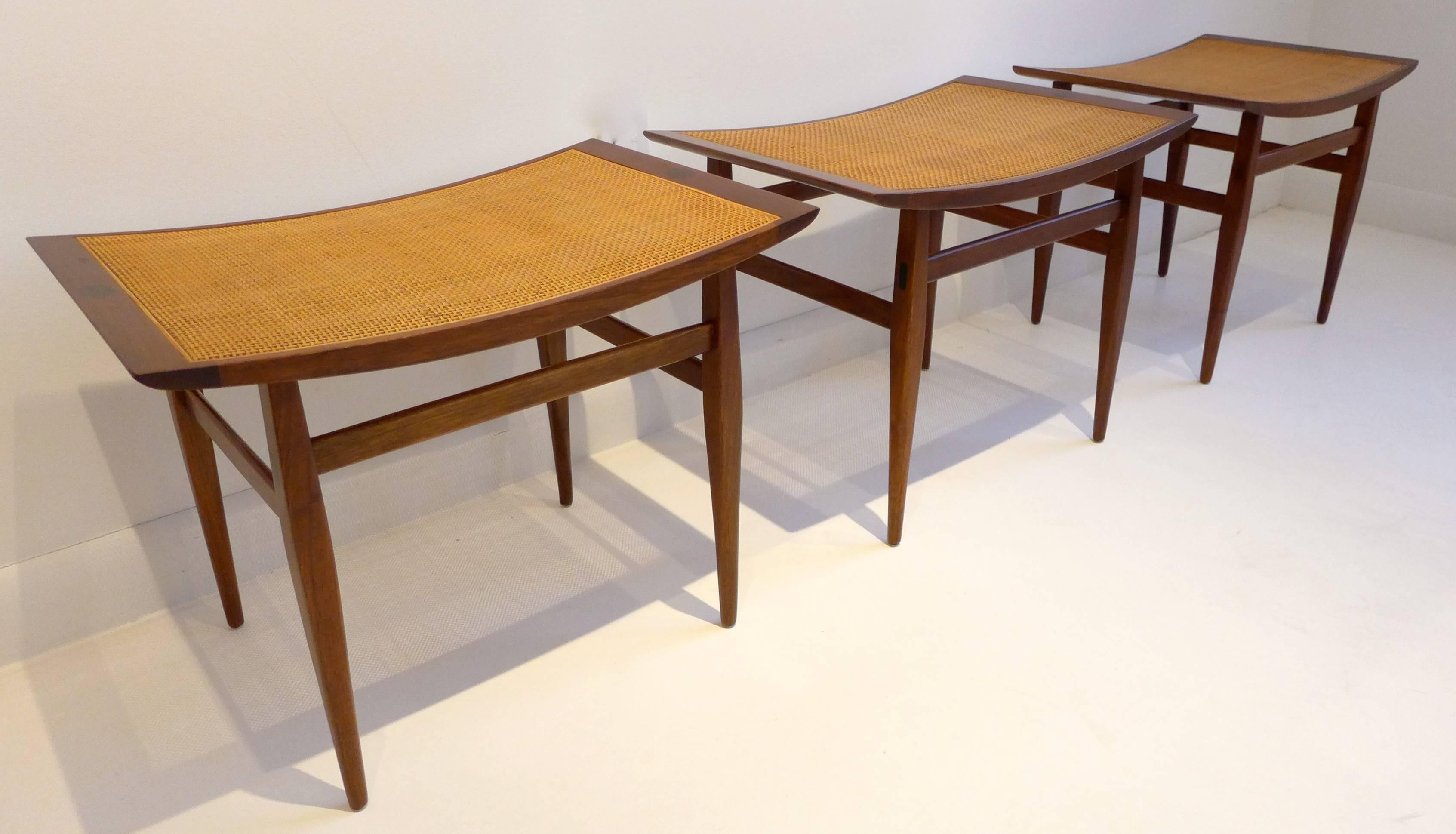 Three stools or benches designed by Kipp Stewart and made by Calvin Furniture for Directional, circa 1950s. A graceful and beautifully detailed work, with carved walnut legs, curved seats, ebony details and original caning. Priced individually.