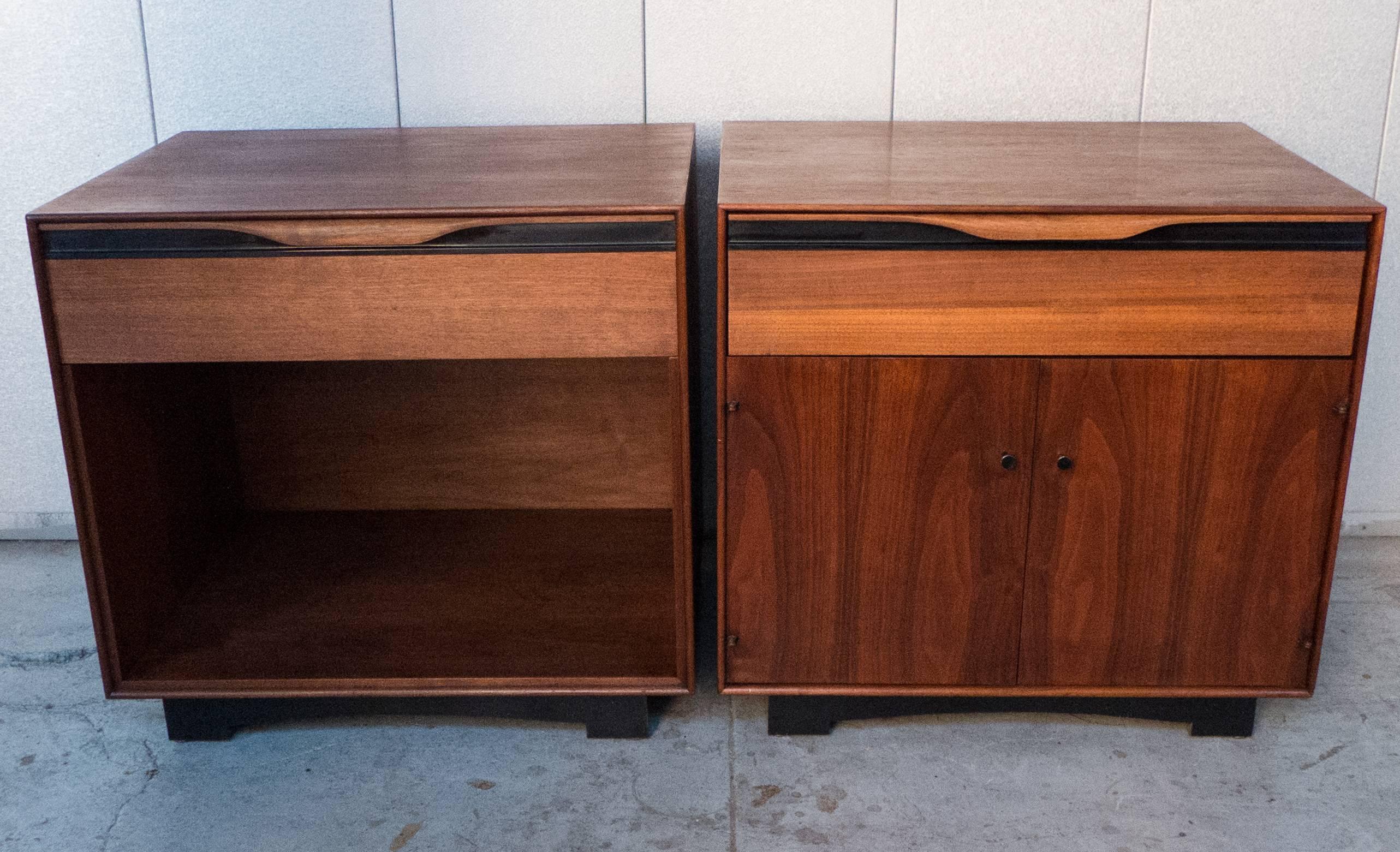 Handsome pair of nightstands in walnut and ebonized wood; one with a drawer with carved scroll pull over an open compartment; the other with a drawer over a pair of doors. Designed by John Kapel for John Stuart, circa 1950s. The differing facade