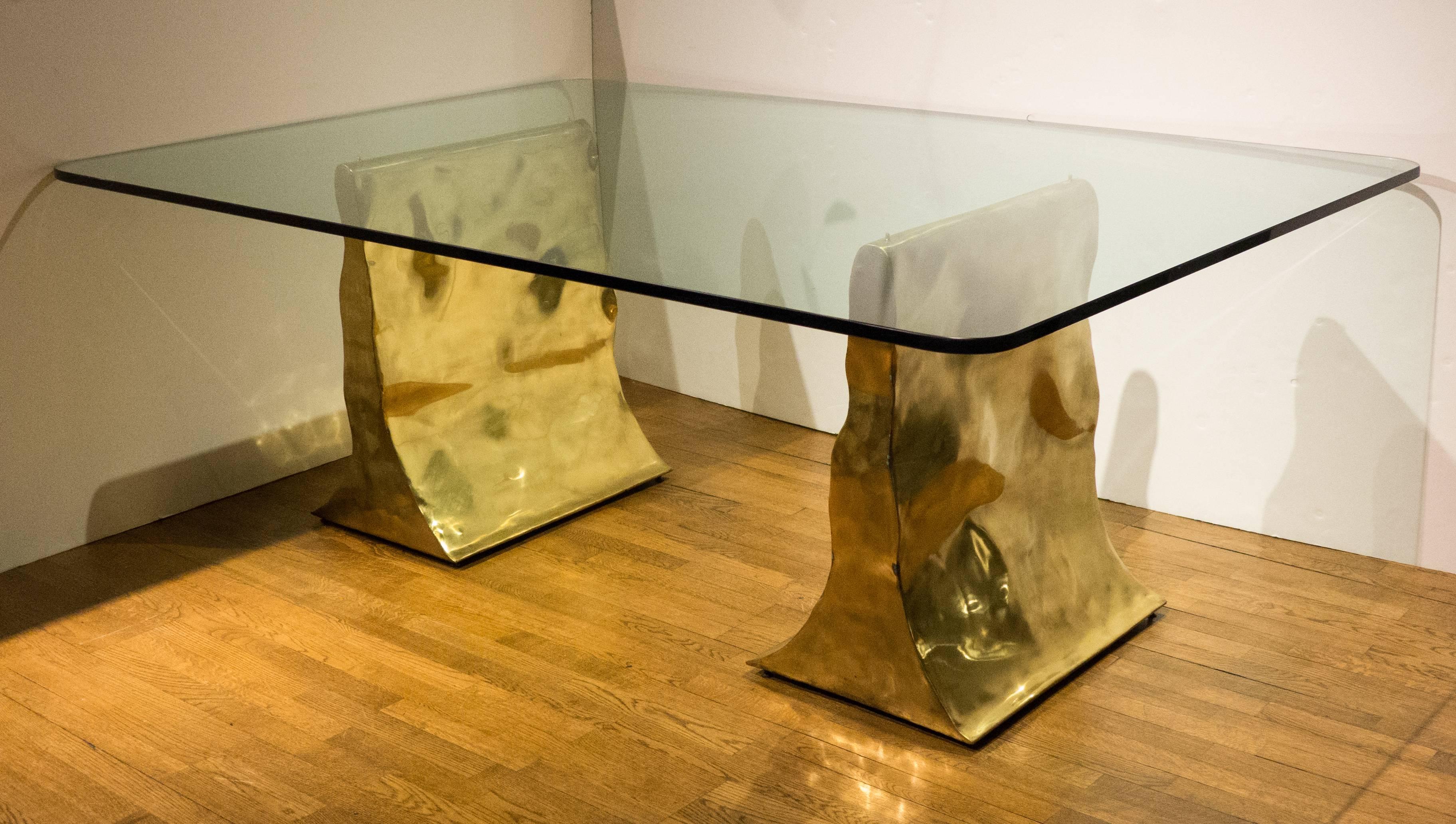 Dining table comprising two sculptural brass bases with a large three-quarter inch thick glass top with polished edges. A rare and impressive work by New York City artist/artisan Silas Seandel, executed in 1982. Each footed base is a unique