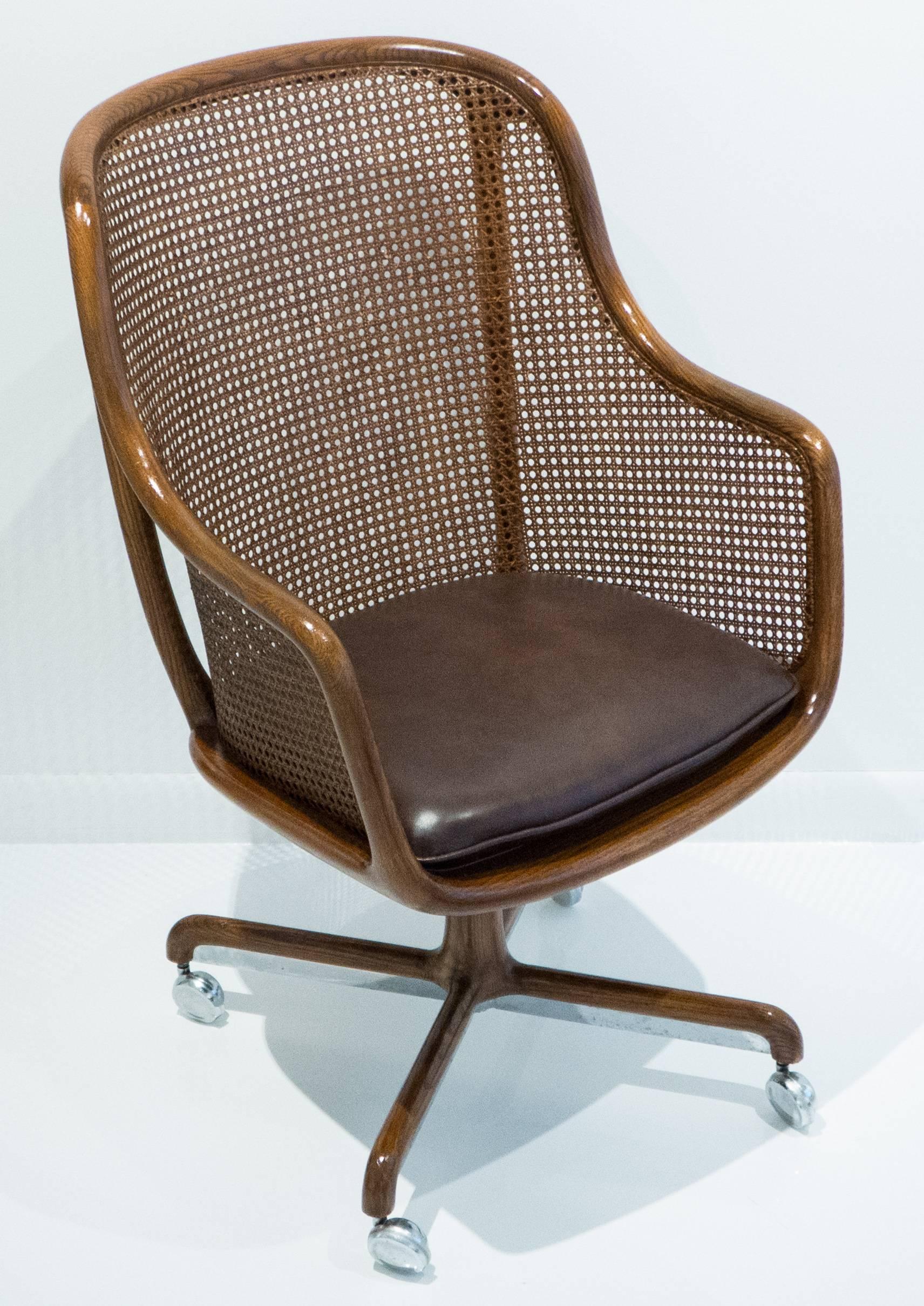 Adjustable, tilt-back office armchair, designed by Ward Bennett for Brickel Associates, circa 1975. Sinuous solid oak frame with original caning, chrome runners and new leather seat cushion. Retains original paper label.