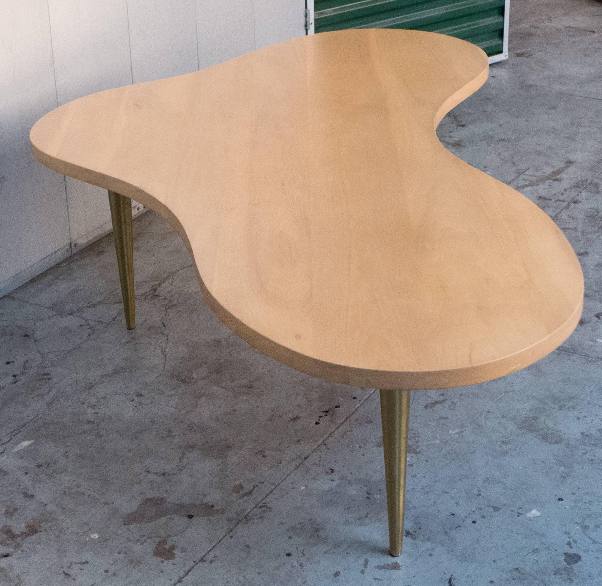 Large biomorphic tripod cocktail table of birch with tapering brass legs. An iconic T.H. Robsjohn-Gibbings design produced by Widdicomb Furniture. With original labels underneath, dated in stencil to December of 1950, making this an early example