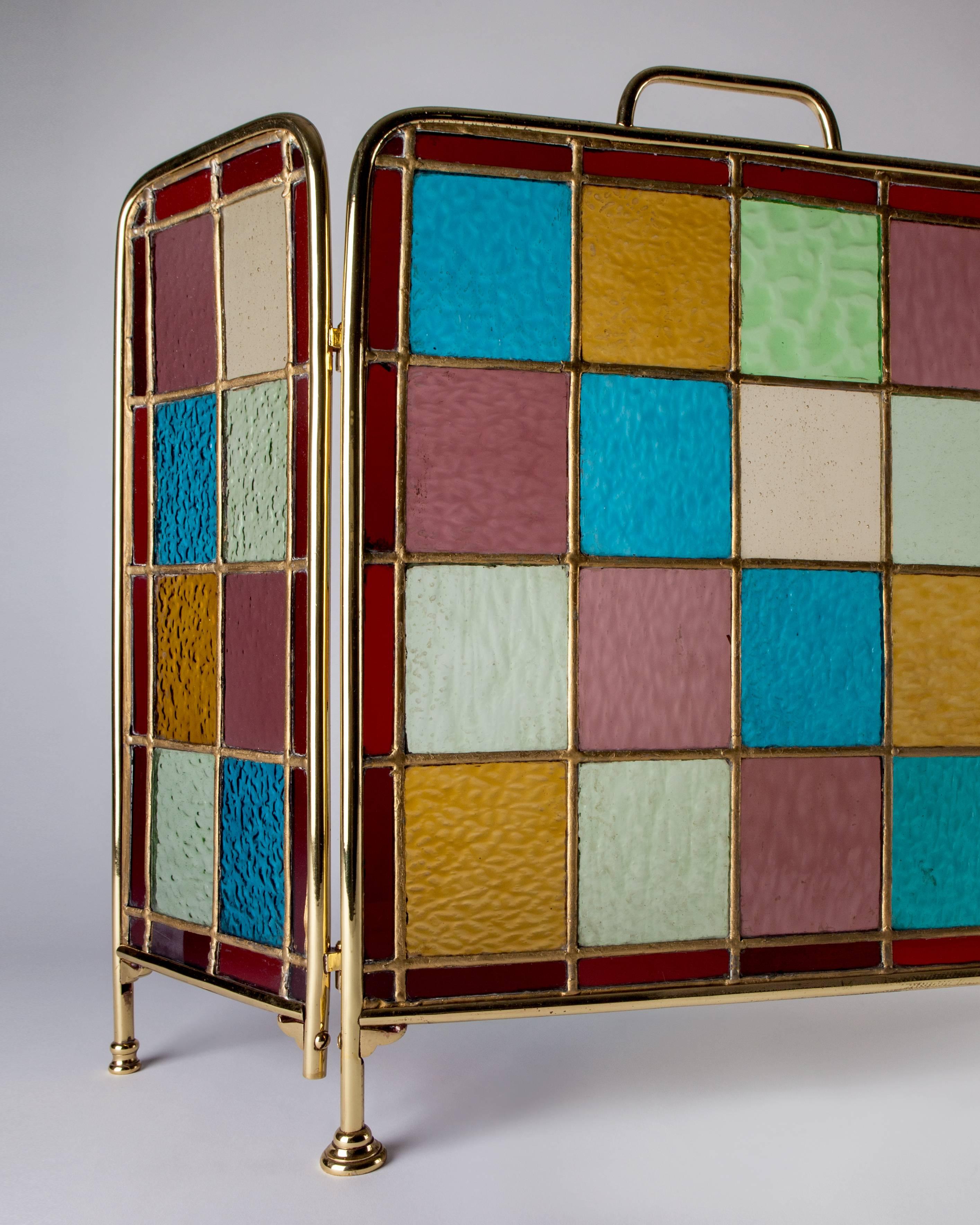 AFP0518.
An antique English fireplace screen in aged brass with leaded glass panels in amber, lavender, blue, green, and pale yellow. Due to the antique nature of this fixture, there may be some nicks or imperfections in the