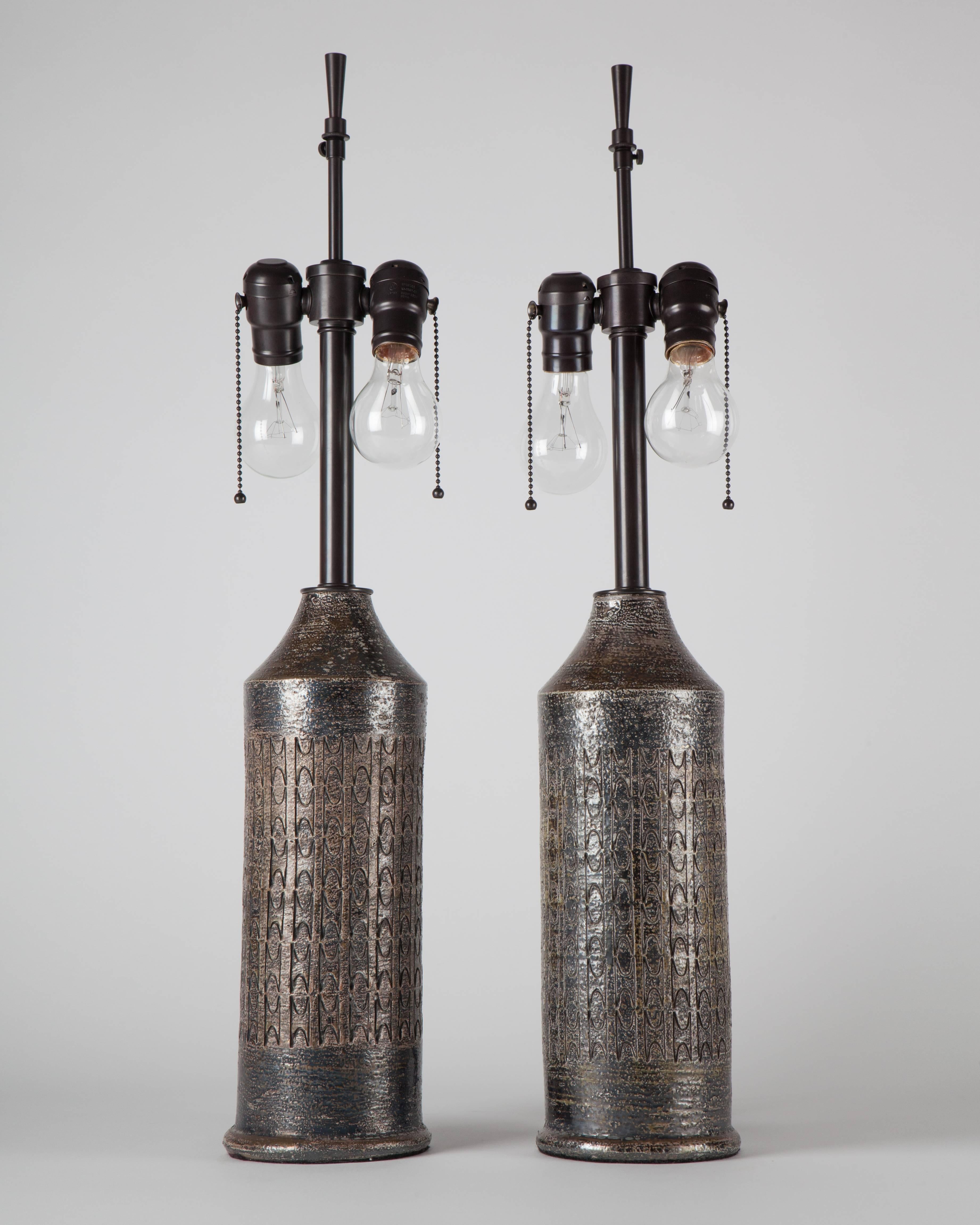 ATL1945

A pair of ceramic lamps, each having an incised geometric pattern, in a metallic textured glaze with darkened brass fittings. Signed by the Swedish marker Bergboms. Due to the antique nature of this fixture, there are some nicks or