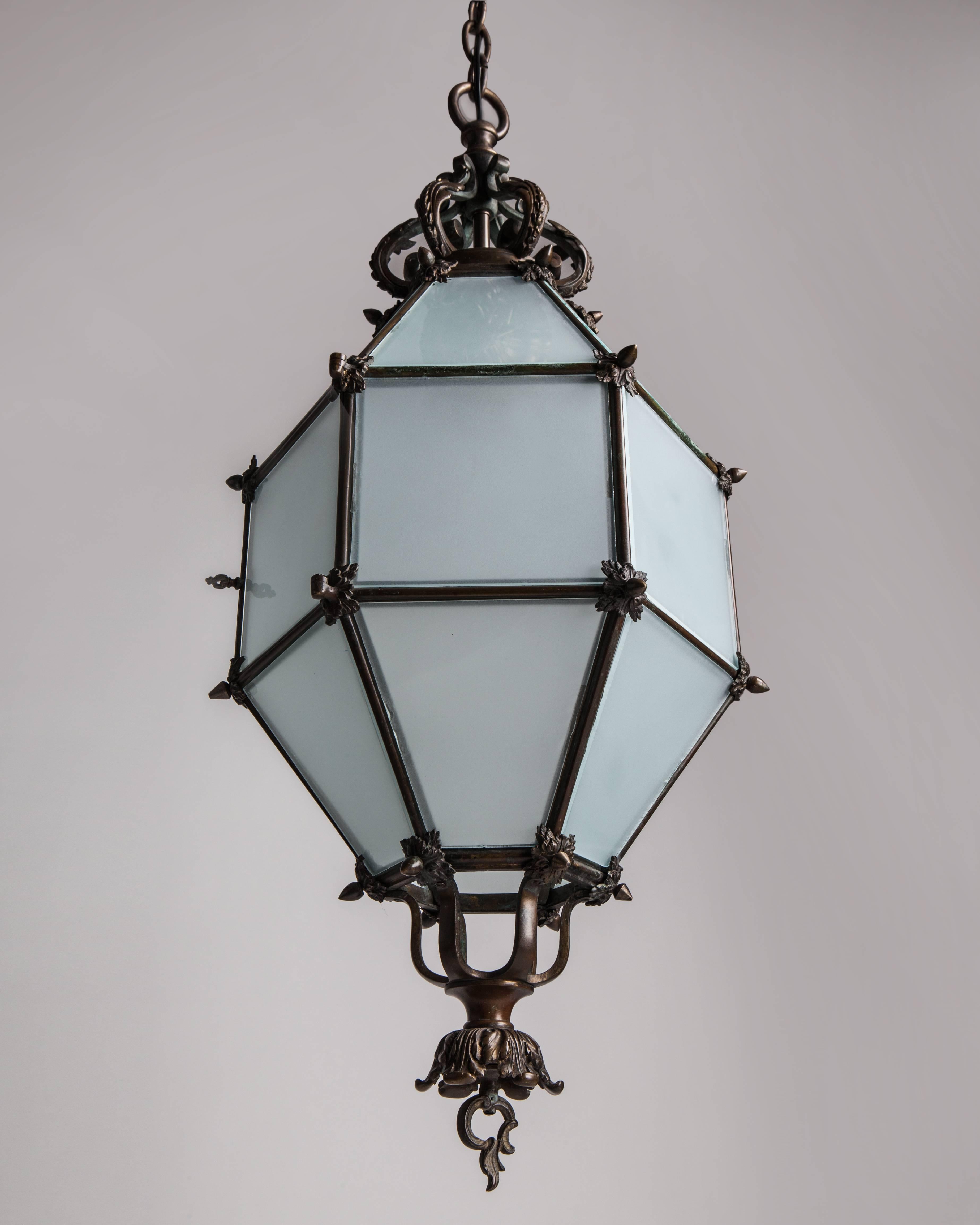 AHL3965.
An antique bronze lantern with 18 facets in its original age-darkened patina. Glazed with frosted glass panels, each secured on the corners with cast foliate pieces. Relamps through a discrete hinged door.

Dimensions:
Current height