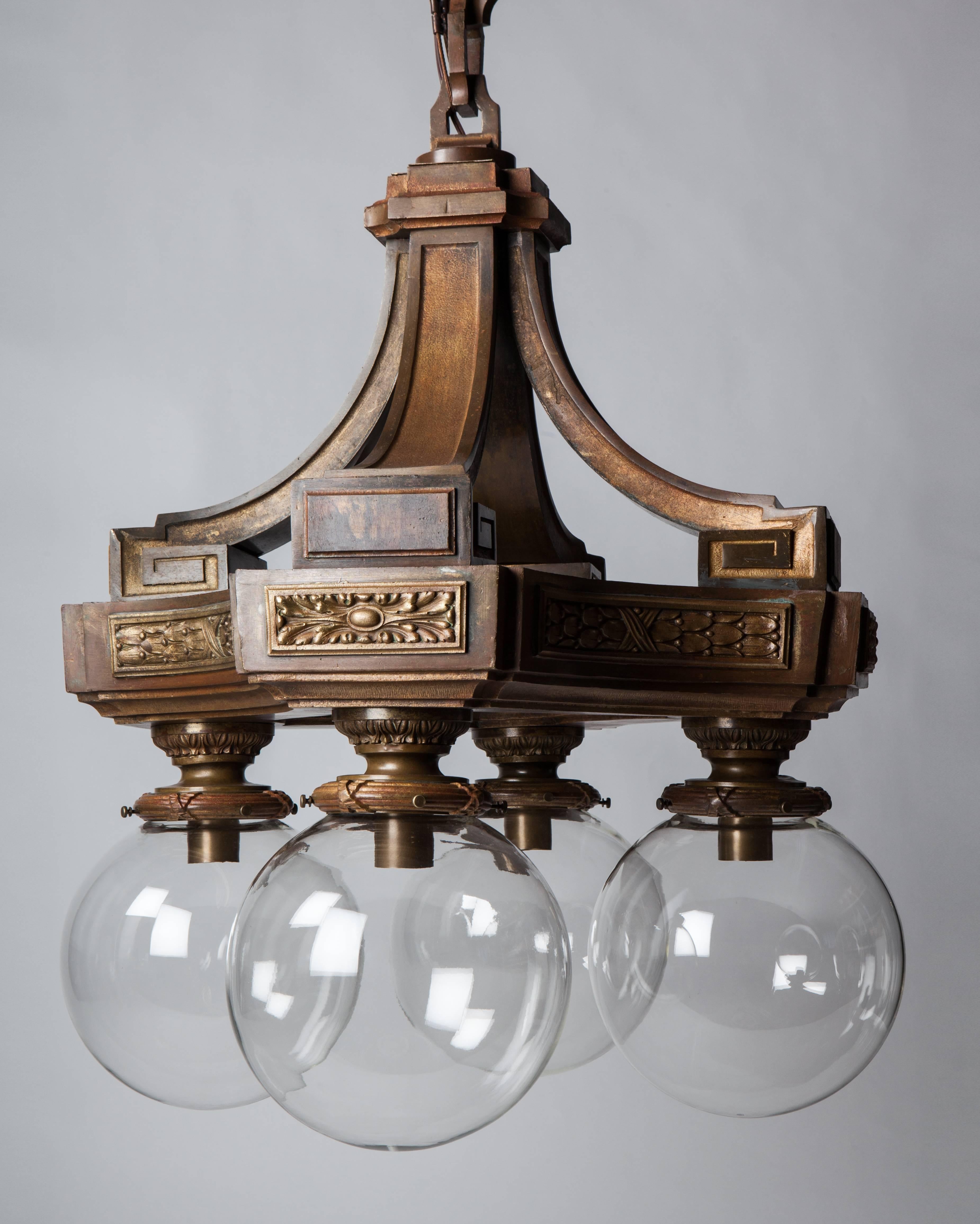 AHL3977.
A gutsy and massive four-light lantern chandelier with Beaux Arts detailing, in its original aged bronze finish, with clear glass shades on its four arms. Due to the antique nature of this fixture, there may be some nicks or imperfections