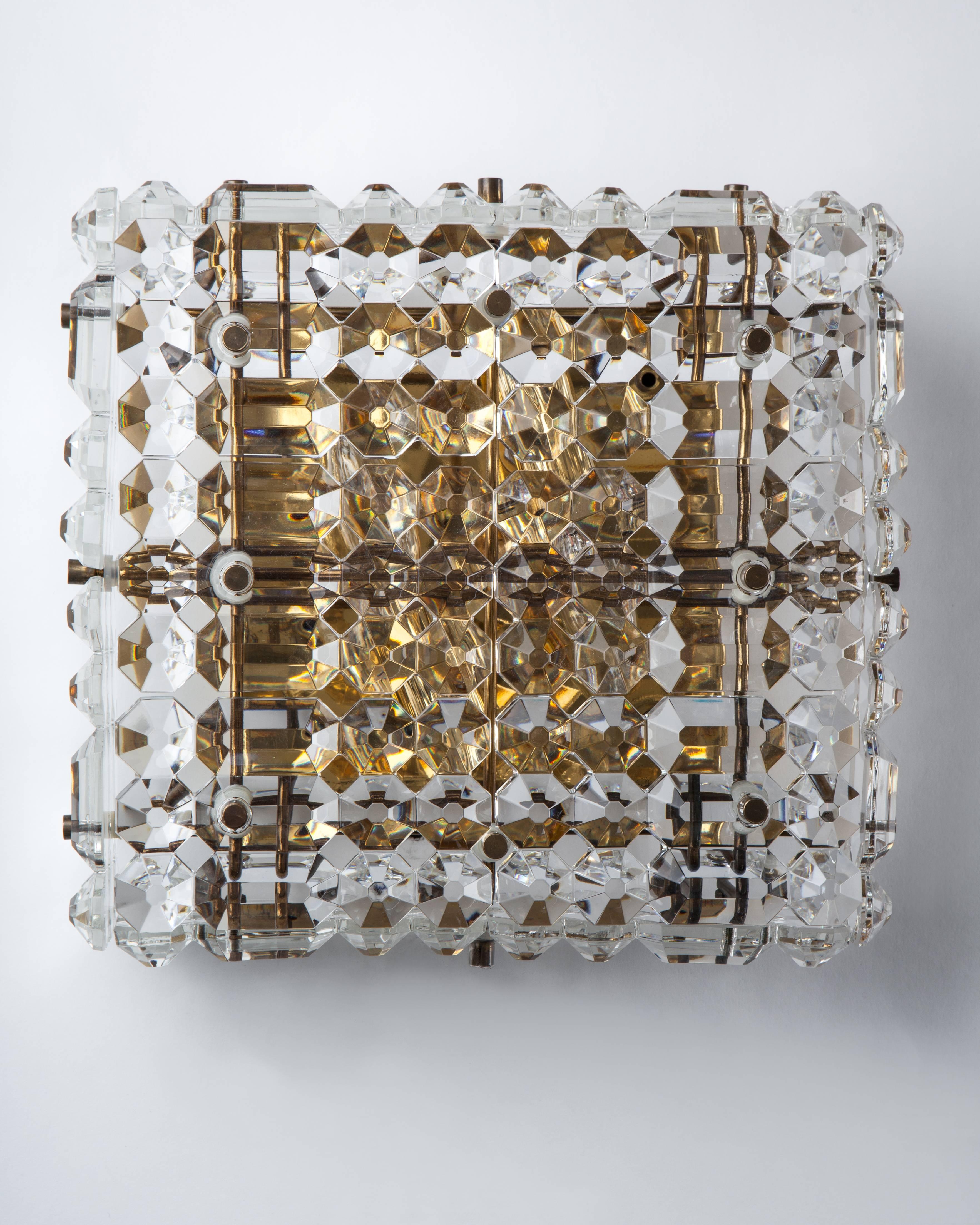 AIS2950.
A pair of quilt-patterned square sconces with tiles of thick clear glass held in a dore brass frame. The body cants slightly forward. This mid century modern fixture is attributed to the Austrian maker Kinkeldey. Due to the antique nature
