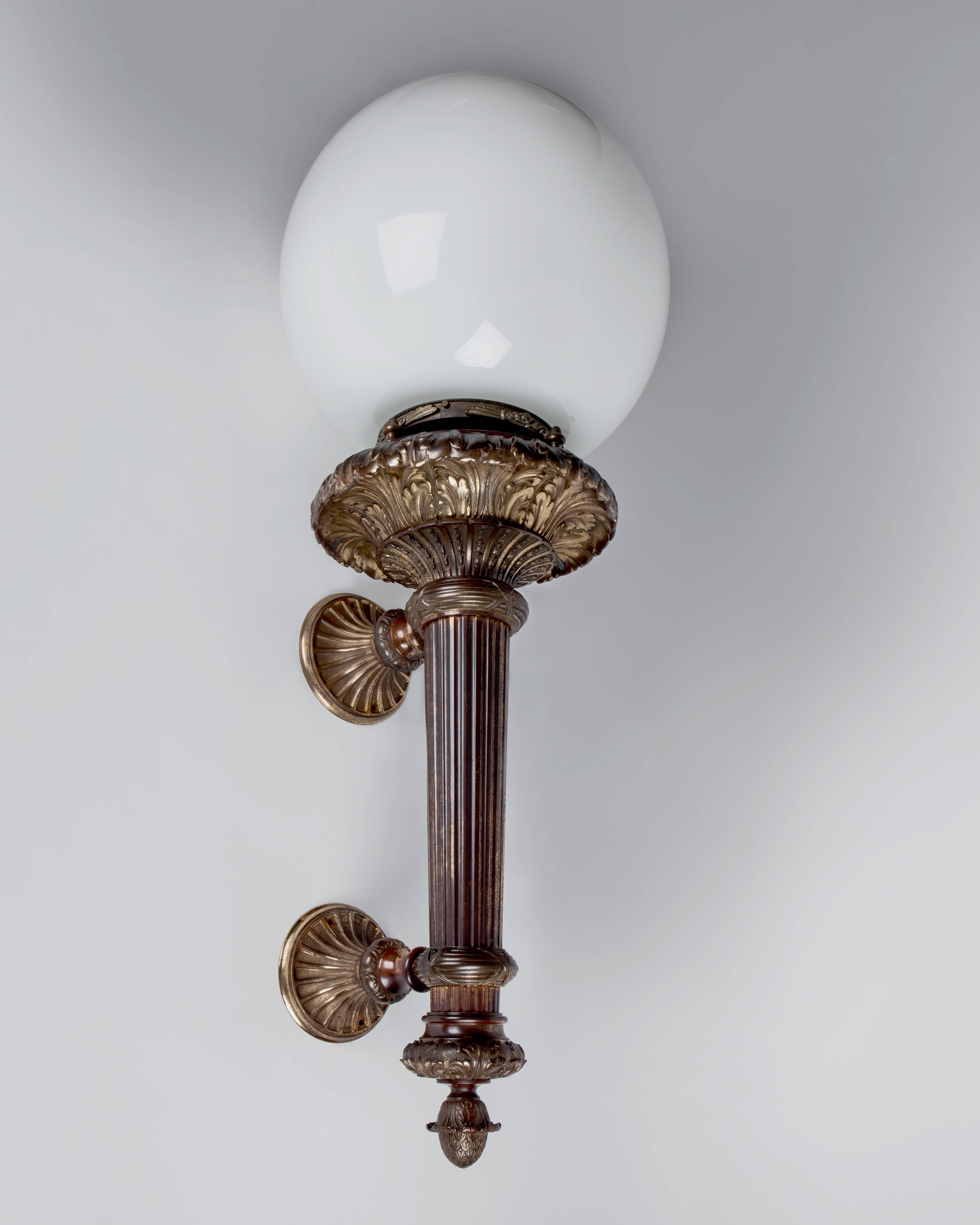 AEX0397
A pair of large antique empire style cast bronze column form exterior wall sconces with fluting, reeding, and foliate details. Each fixture is finished with a large opal white glass shade. From a Youngstown, Ohio commercial