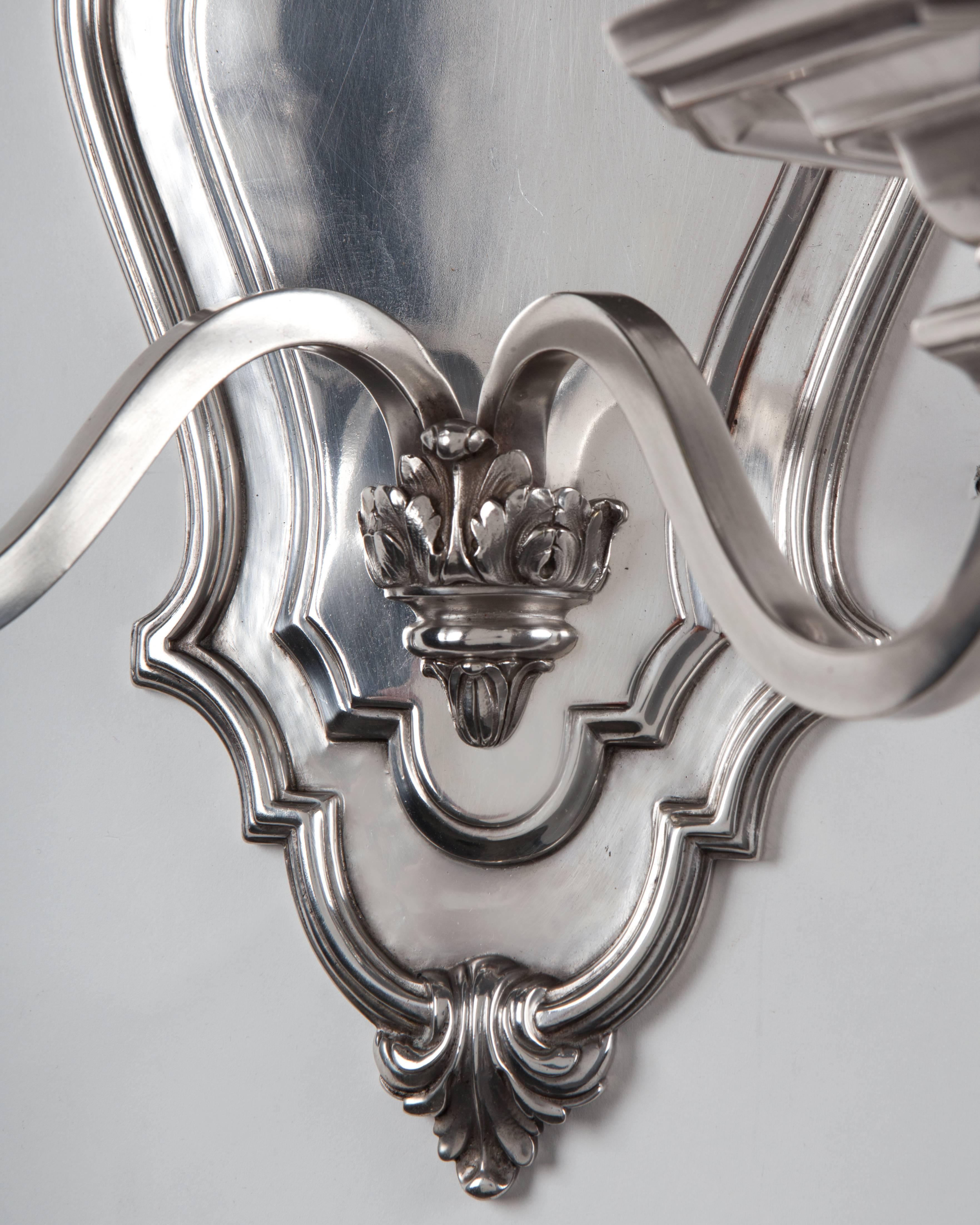 AIS2966.
A pair of silver plate double-light sconces with shallow, scalloped-edge backplates. Square-section S-curving arms spring from the backplate to support chamfered square bobeches and faceted candle cups. Signed by the New York maker E. F.