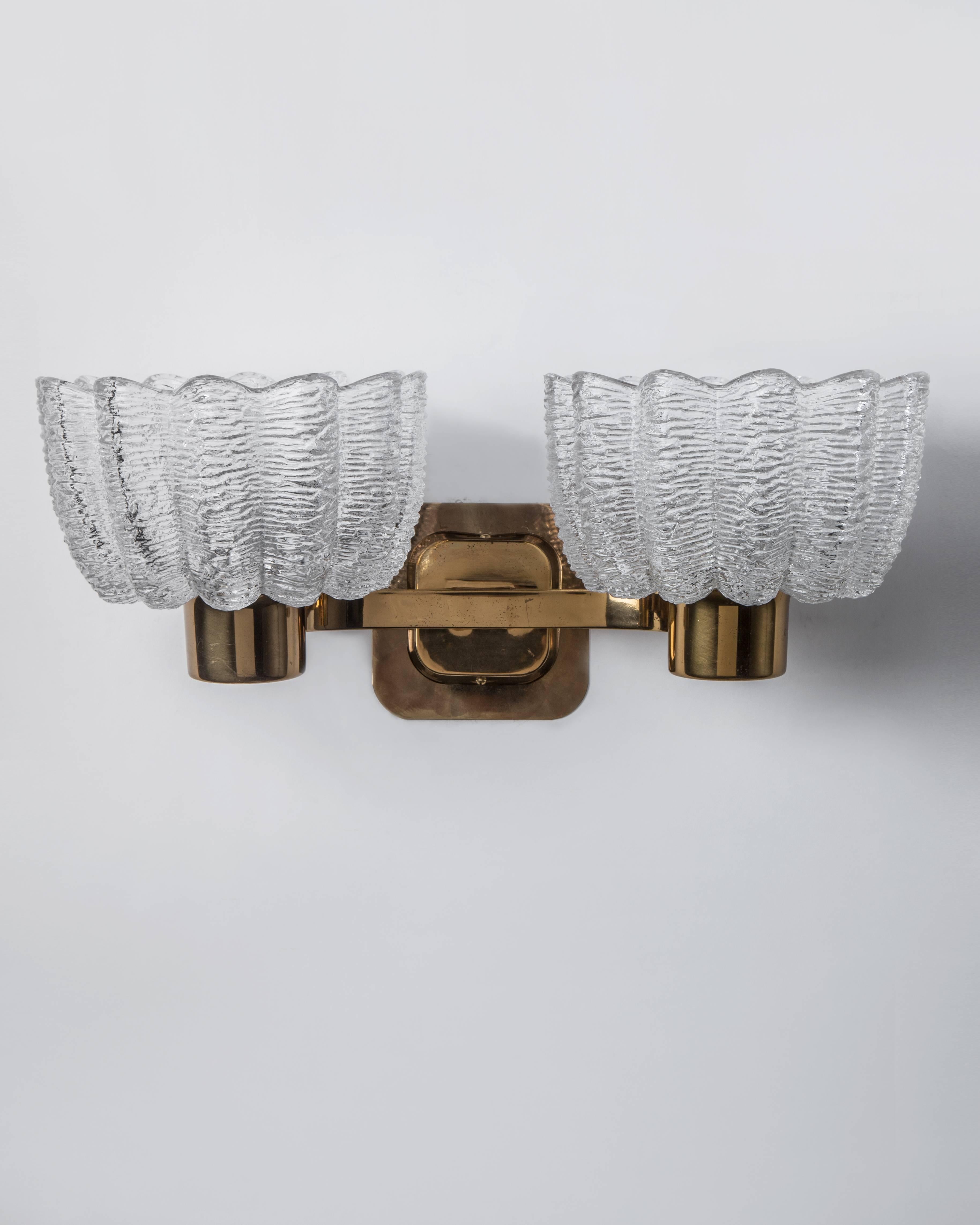 AIS2973.
A pair of vintage mid century modern sconces with thick, clear textured lobed glass shades and aged brass metalwork. Due to the antique nature of this fixture, there may be some nicks or imperfections in the glass.

Dimensions:
Overall: