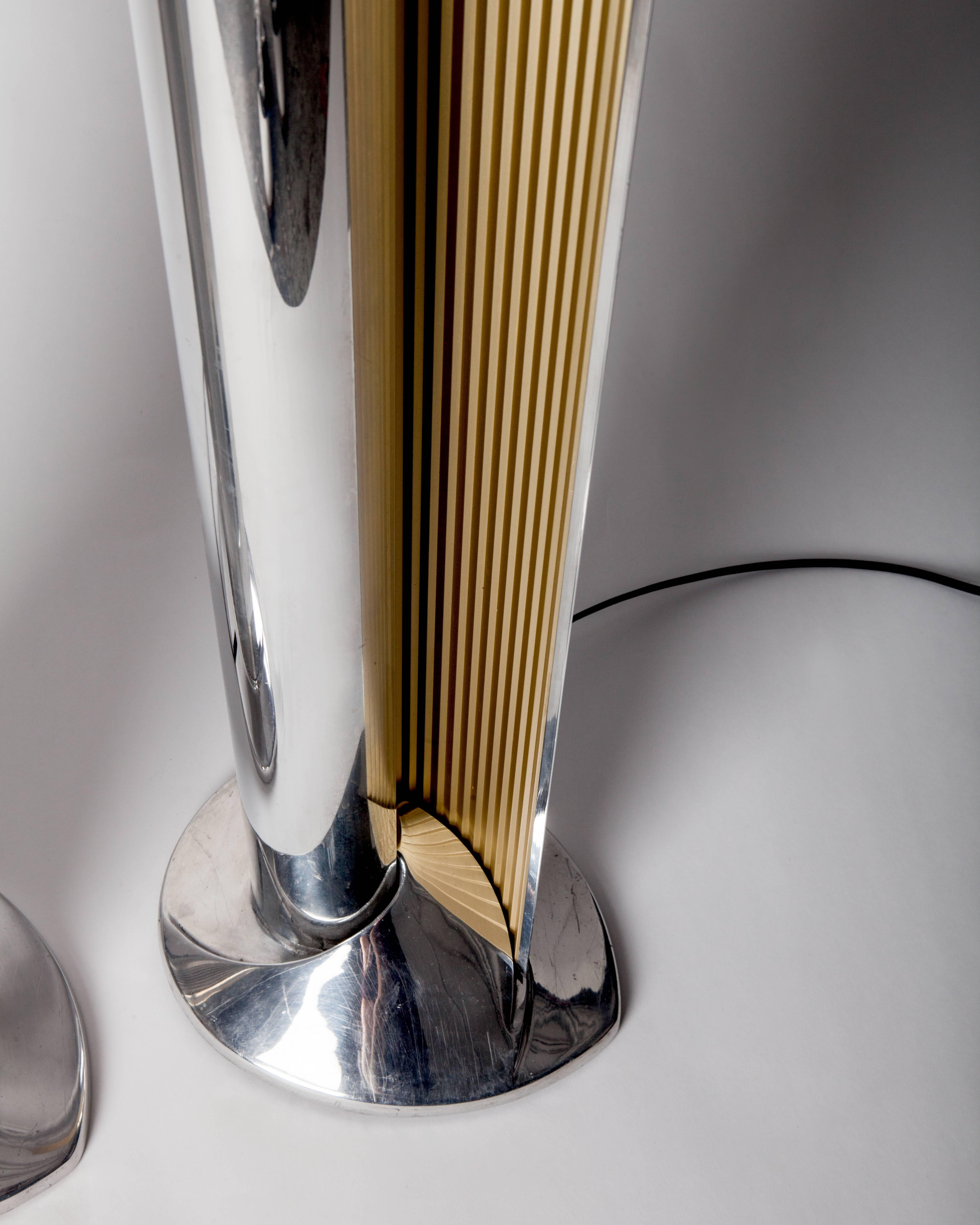 AFL1833.
A pair of tall vintage floor lamps in polished aluminum with serrated gold reflectors. These lamps hold long LED tubes at the center of a nautilus spiral which indirectly casts light via the unfurled opening on teardrop-shaped bases.
