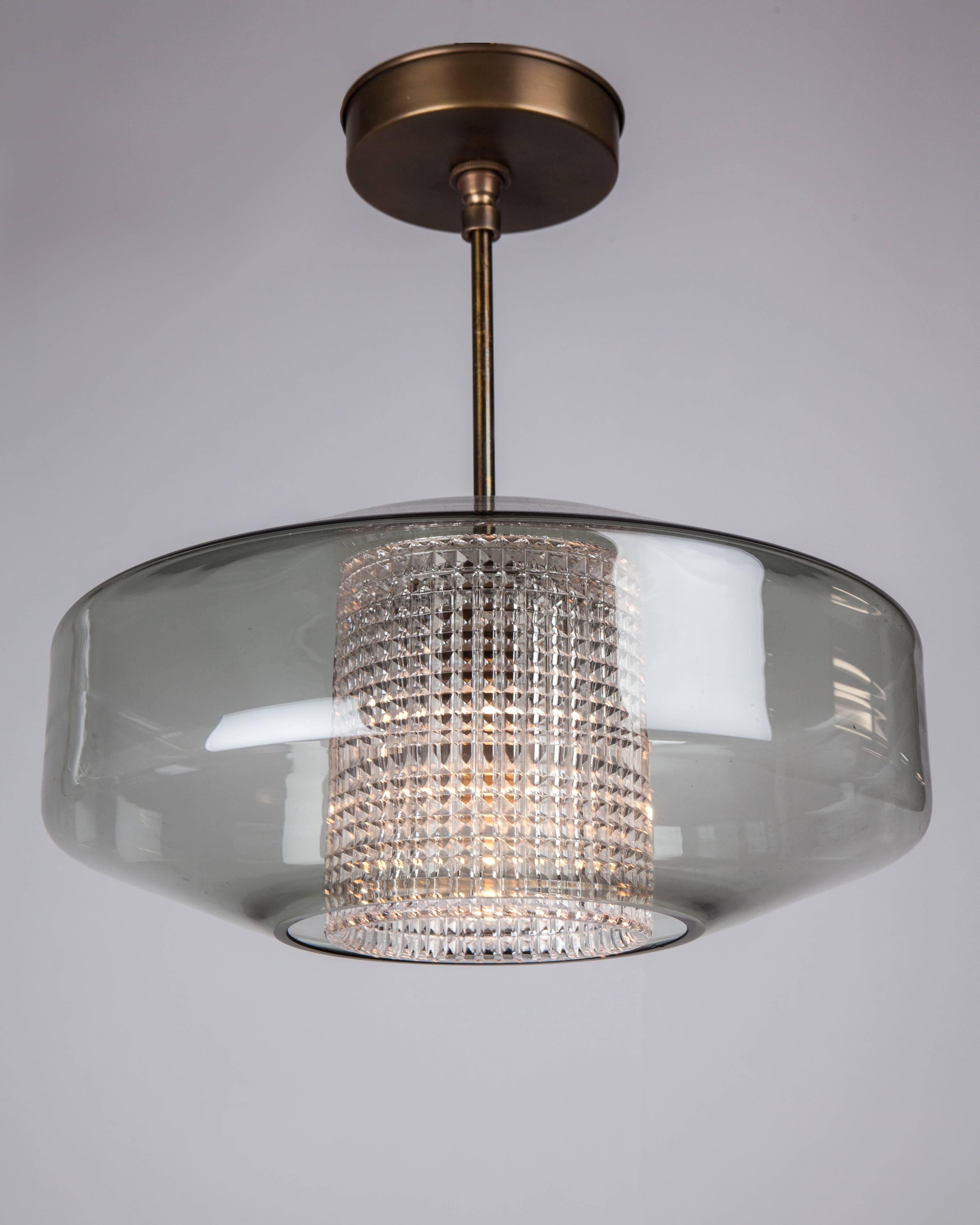 AHL4007
A vintage pendant having a hatched patterned glass core surrounded by a subtle grey saucer, suspended on its original aged brass metalwork. By the Swedish glassmaker Orrefors. Due to the antique nature of this fixture, there may be some