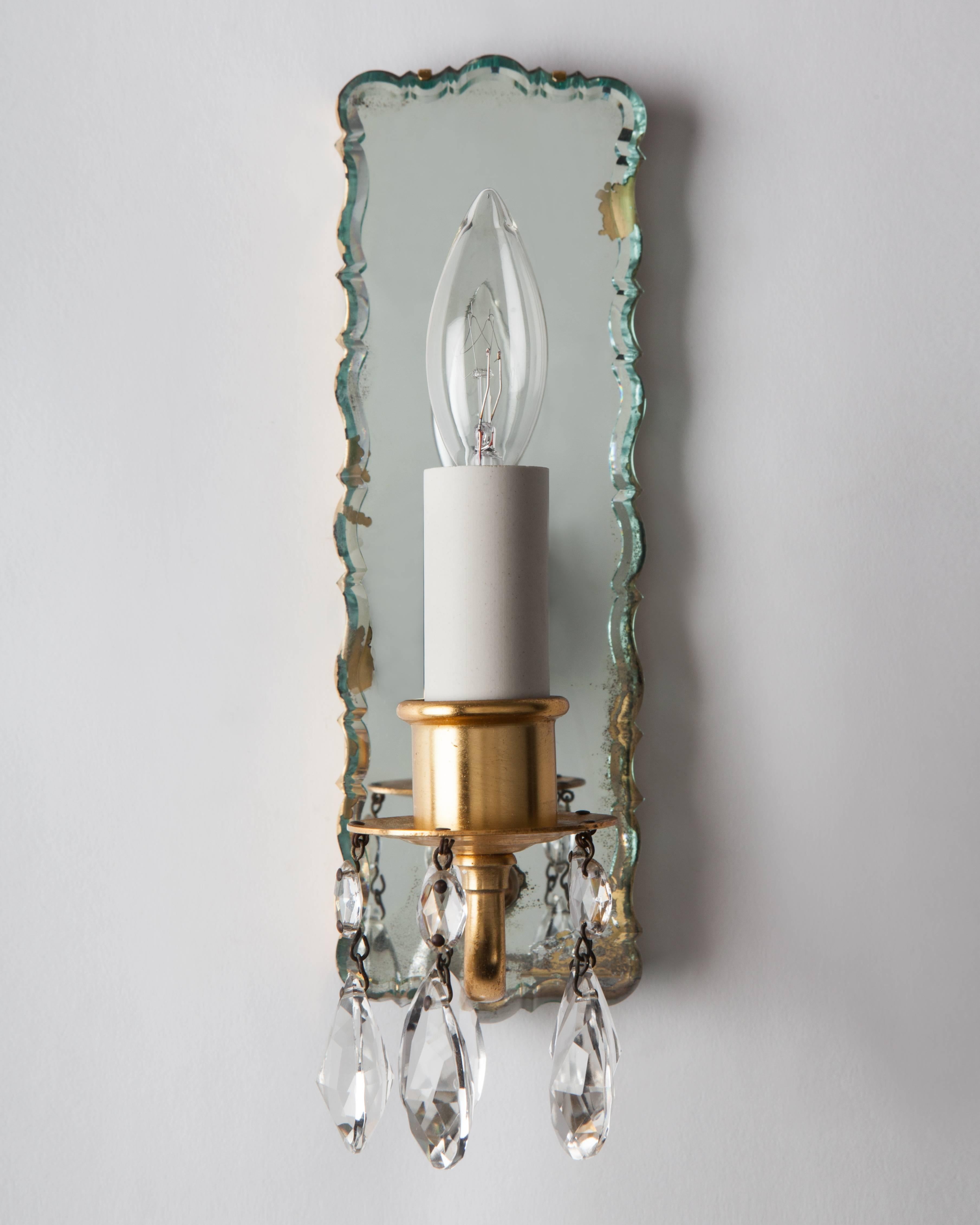 AIS2981
A pair of slender sconces having scalloped, beveled mirrors as backplates and gilded metalwork dressed with prisms. Due to the antique nature of this item there are nicks and imperfections in the glass as well as losses to the