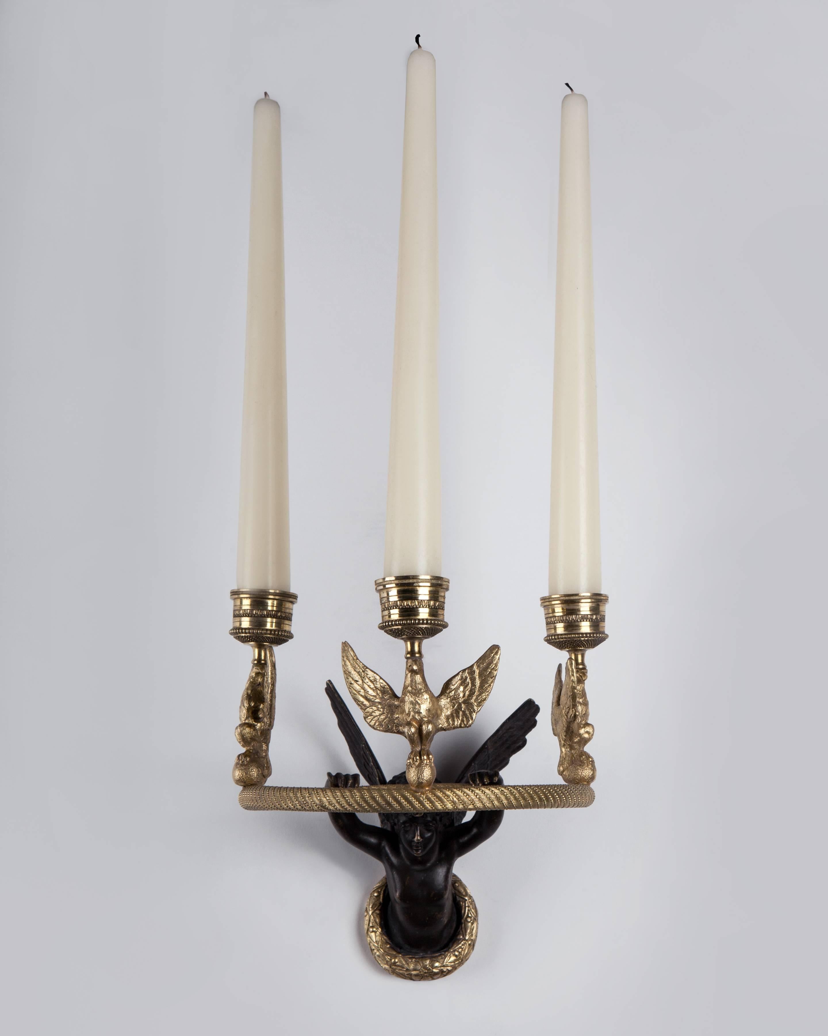 AIS3010

A single gilded and patinated bronze candle sconce composed of a winged cherub or angel figure holding a fine, spiral bead-wrapped, reeded hoop, mounted with three eagles holding candle cups.

Dimensions:
Overall: 6-1/2
