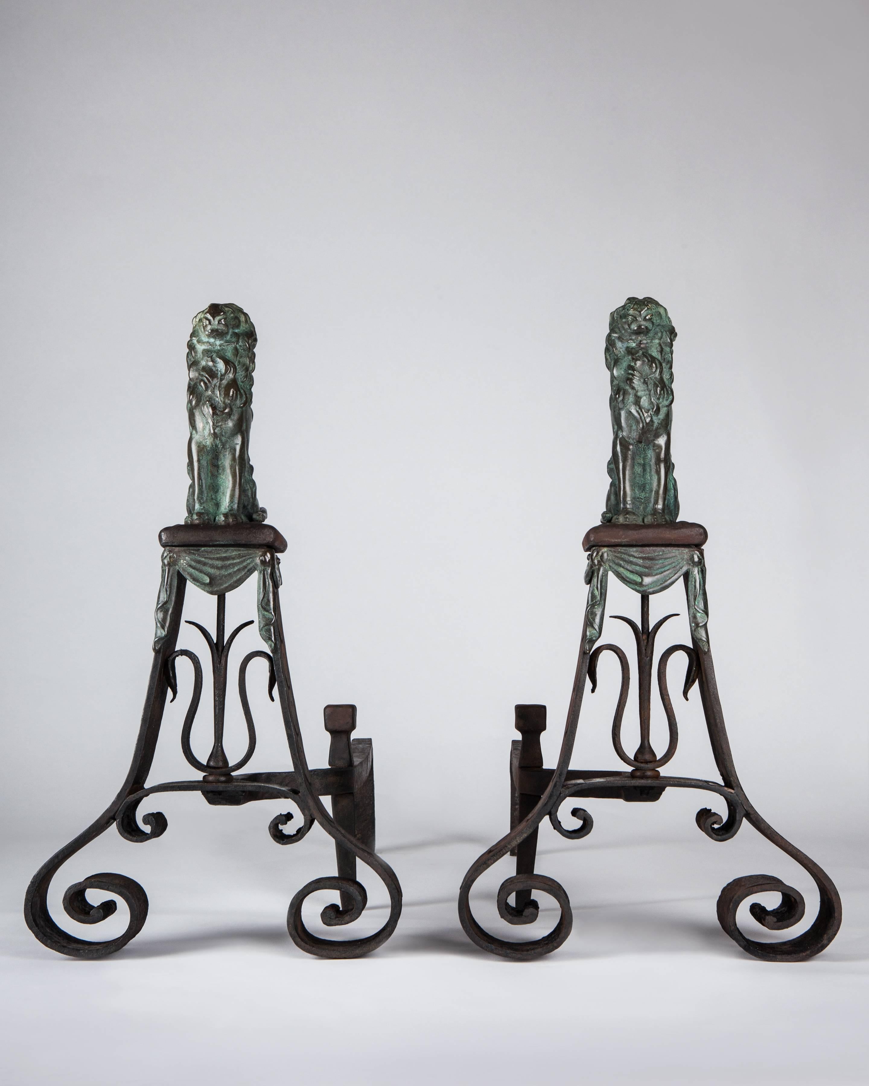 AFP0593
A pair of antique wrought iron and bronze andirons having exaggerated scroll-footed bases with imbricated chiseled details. Mounted to the iron are cast bronze drapery swags trailing beneath shallow pedestals, surmounted by large seated